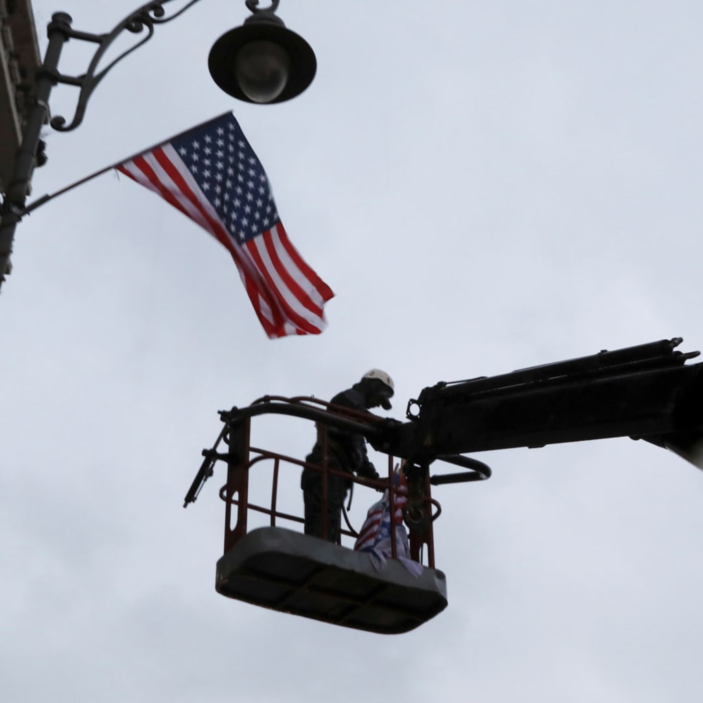 <p>A laborer hangs a U.S. national flag on a lamp post along a street where the U.S. consulate in located in Jerusalem on December 6, 2017. </p>

