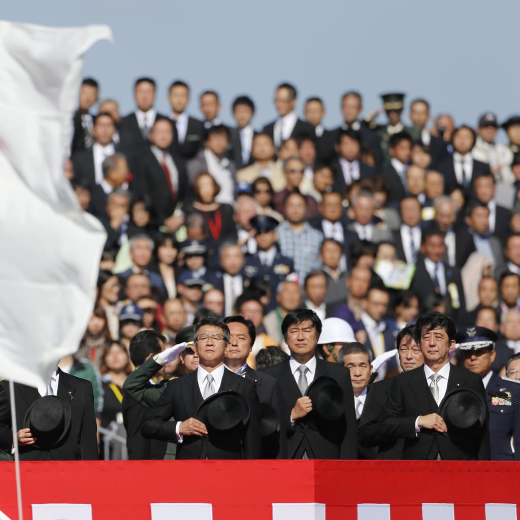 Japanese Prime Minister Shinzo Abe salutes Japan's national flag as he reviews Japan Self-Defence Forces troops during an annual ceremony at Asaka Base in Asaka on October 27, 2013.