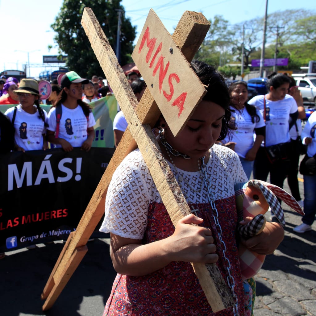 An activist carries a cross during a march to mark International Women's Day in Nicaragua on March 8, 2018.The banner reads "Not one more. No more violence against women."