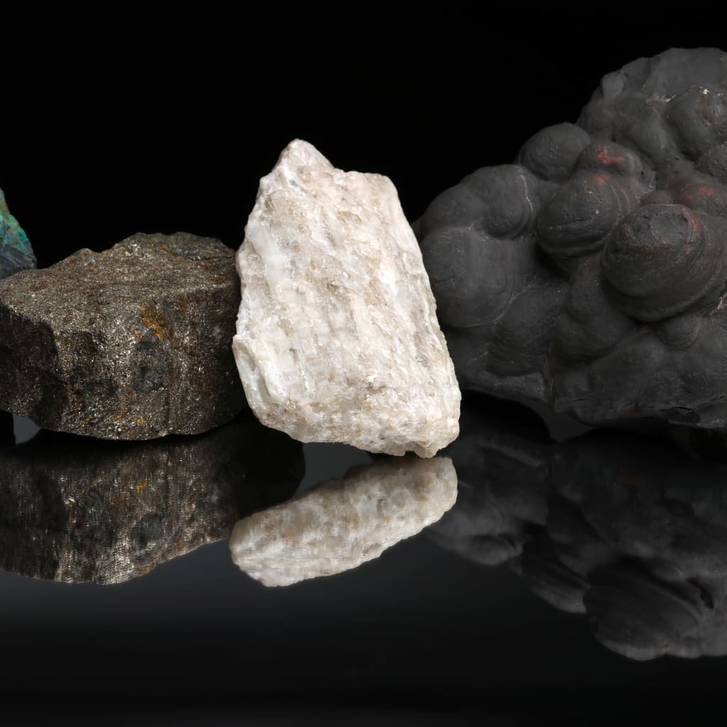 Critical mineral ores, including copper, graphite, nickel, lithium, and manganese, against a black background and reflected on a mirrored table.
