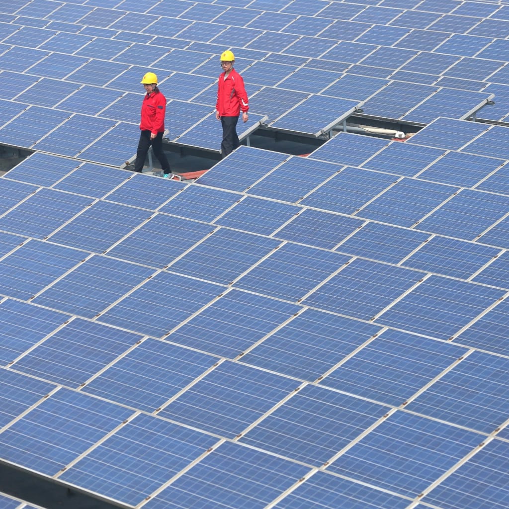 Workers walk past solar panels in Jimo, Shandong Province, China
