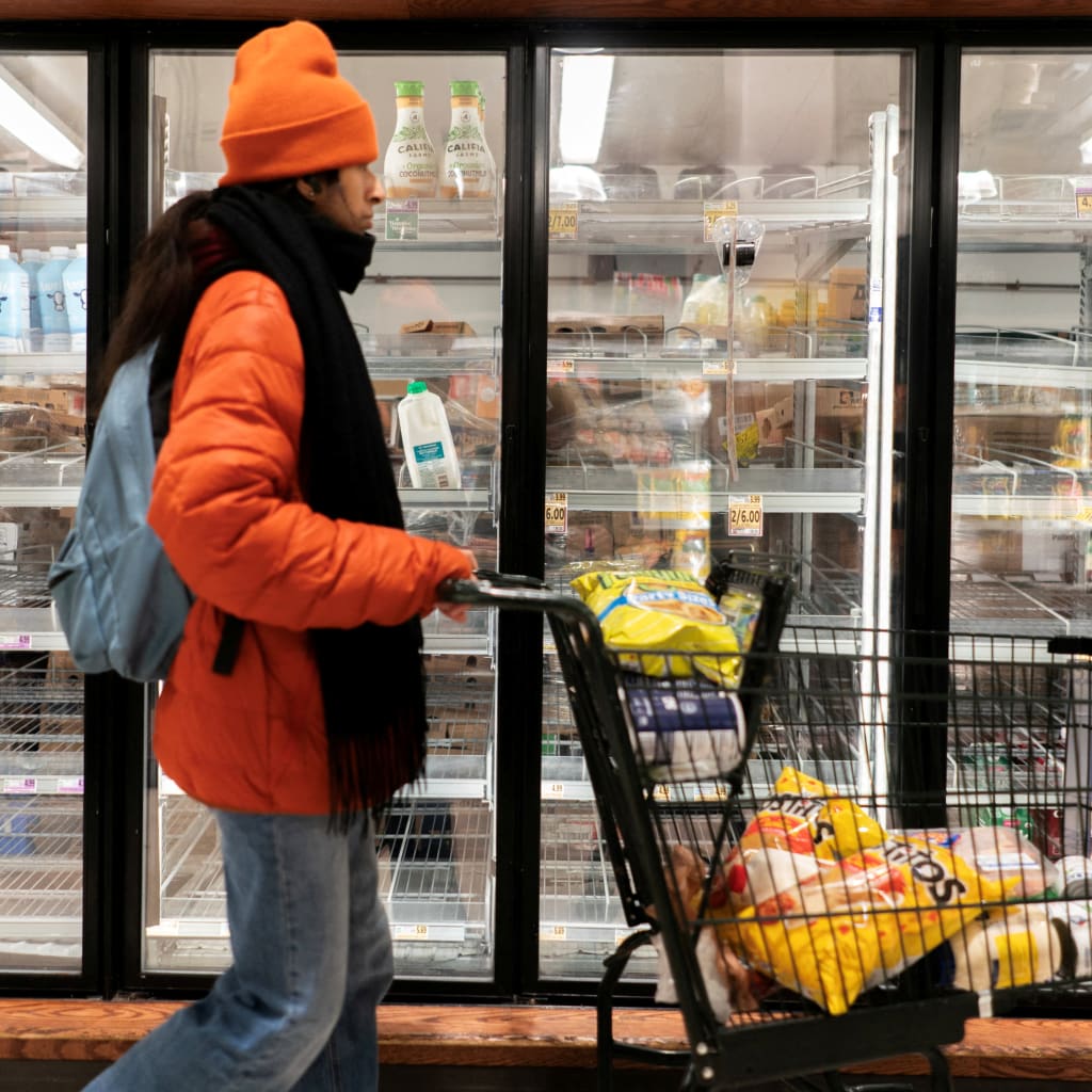 A shopper walking past a partially empty dairy section of a grocery store