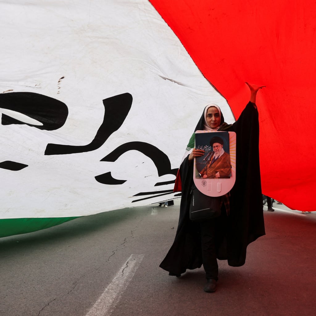 An Iranian woman holding a poster depicting Iran's Supreme Leader Ayatollah Ali Khamenei walks under a large flag during the forty-seventh anniversary of the Islamic Revolution in Tehran, Iran on February 11, 2026. Majid Asgaripour/West Asia News Agency via Reuters