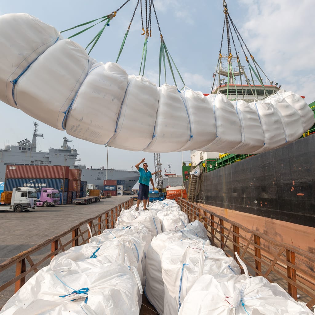 A crane lowers a white package containing food aid into a crate off of the side of a ship.