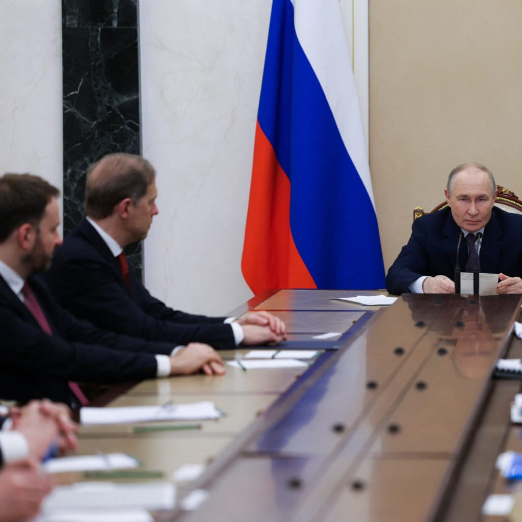 Vladimir Putin sits at the end of a long conference table surrounded by advisors.