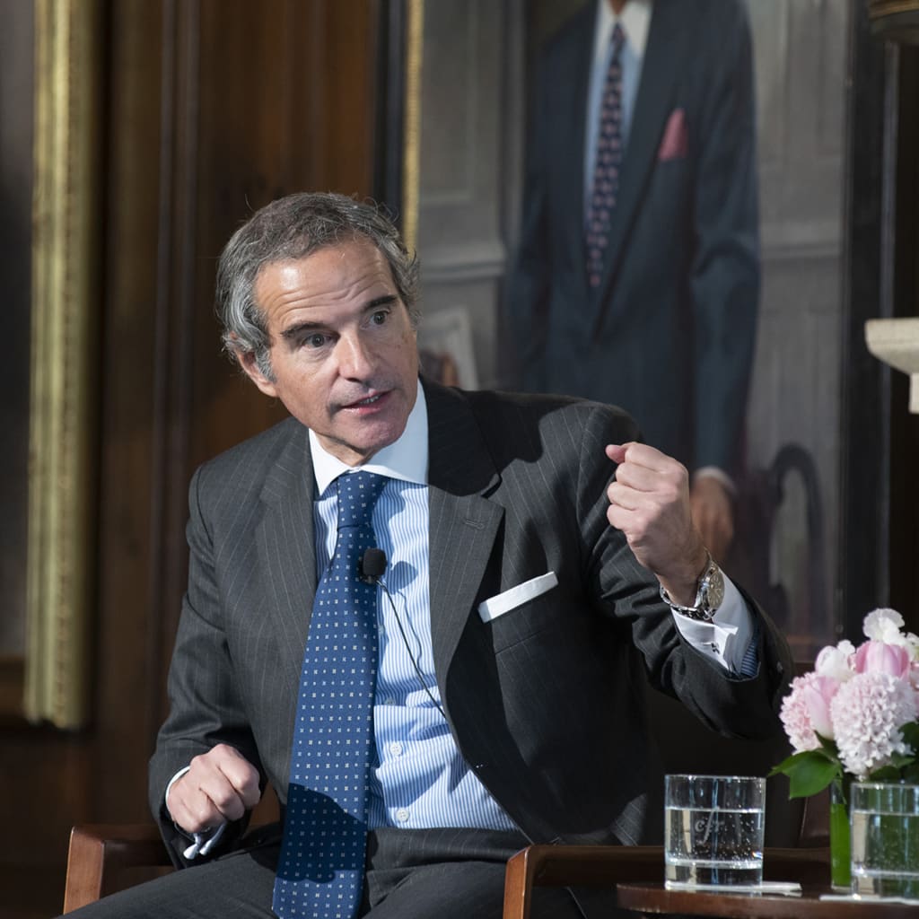 Rafael Grossi sits in a chair, making a hand gesture while speaking during an event.
