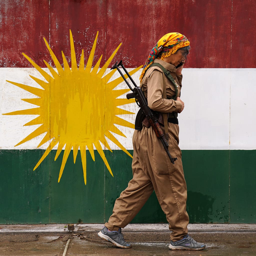 A female soldier walks in front of a Kurdish flag while on the phone