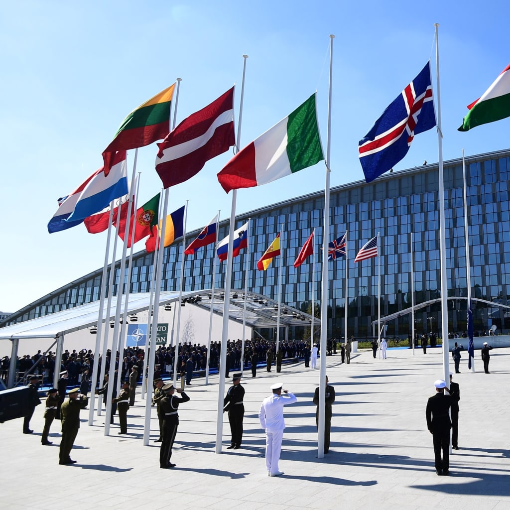 Officials and military personnel stand beneath flags as they attend the NATO (North Atlantic Treaty Organization) summit ceremony at the NATO headquarters, in Brussels, on May 25, 2017.