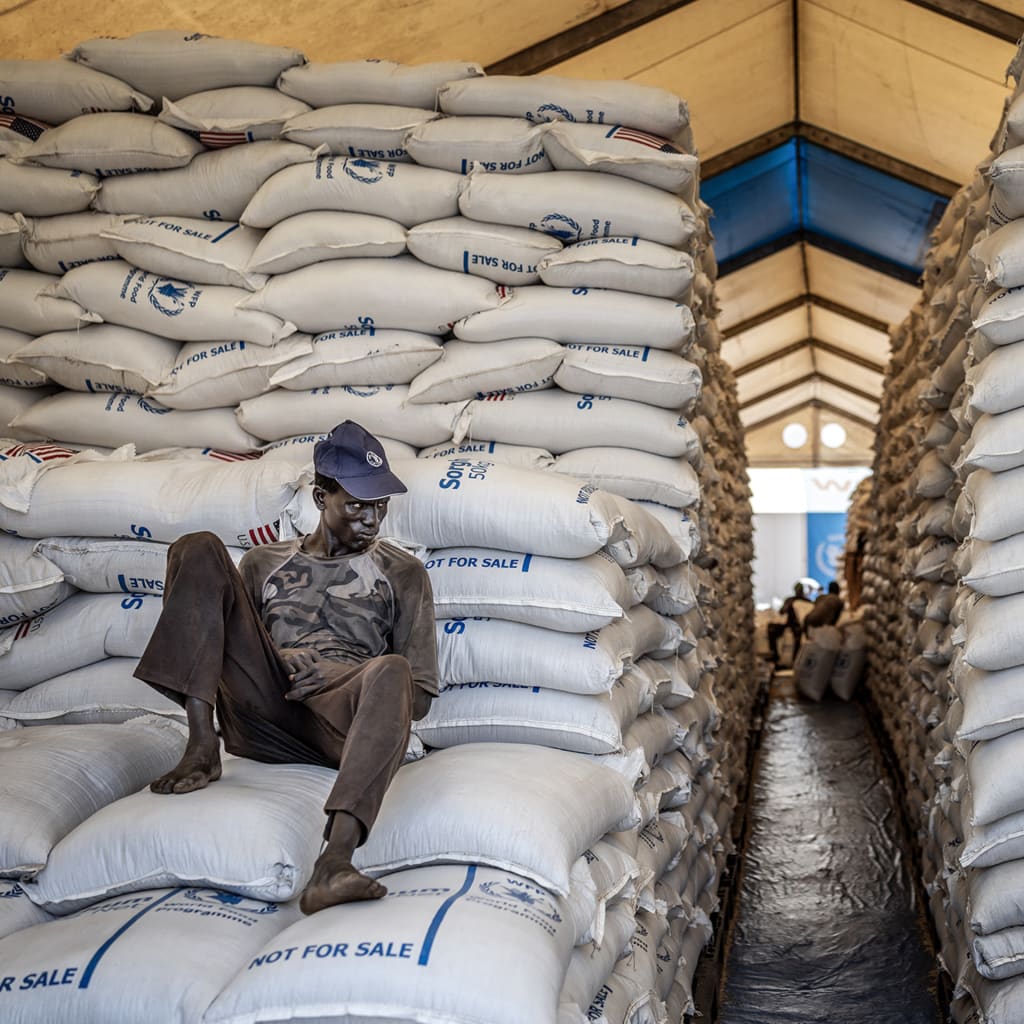 A worker sits atop sacks of food aid in a hangar where supplies are piling up because deliveries are halted due to insecurity from the conflict, at a World Food Programme (WFP) warehouse in Bor, Jonglei State, on February 13, 2026.