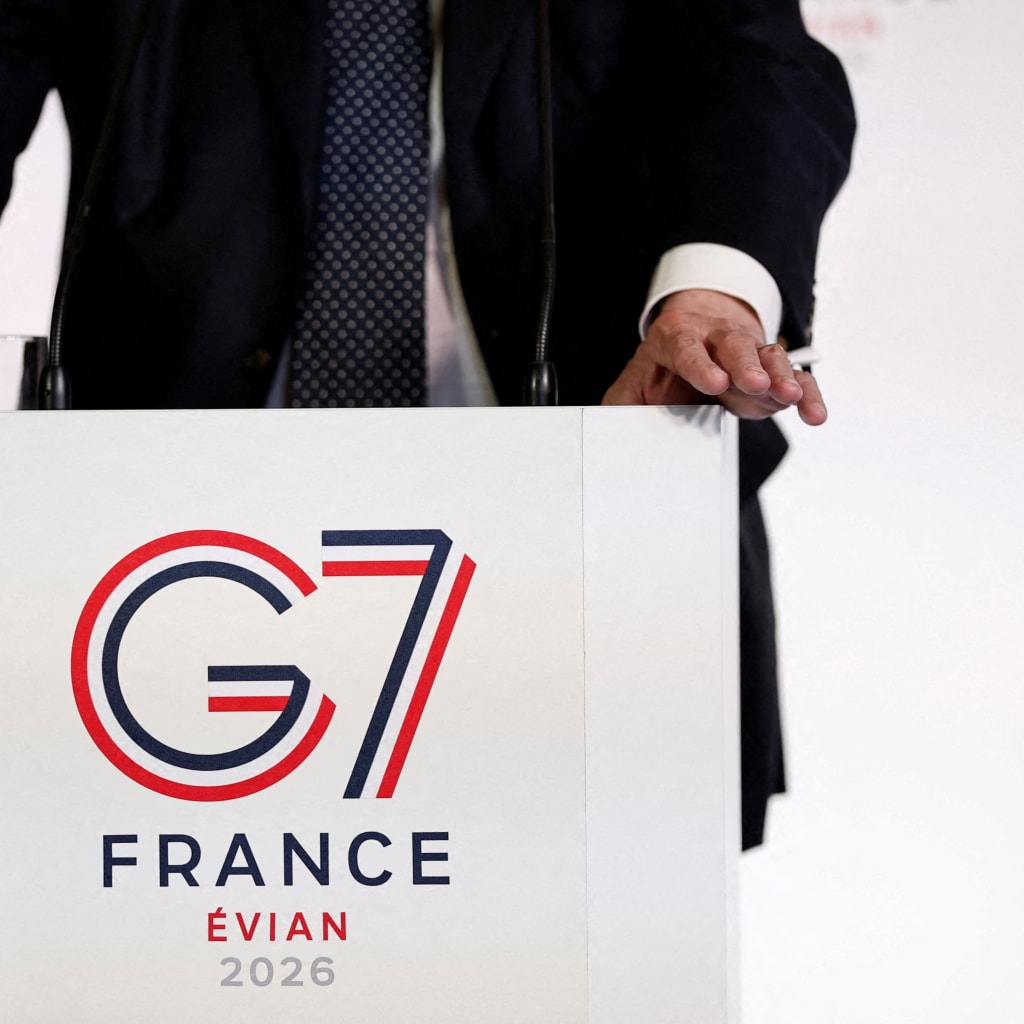 The logo of the G7 Evian summit is seen on a desk with person sitting behind it.