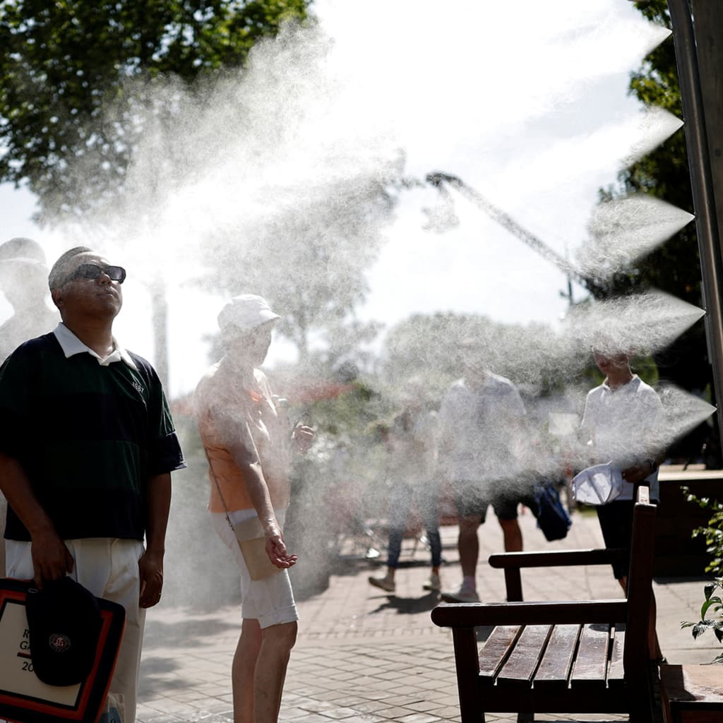 People stand to the left of the photo, and to the right is a machine that is spraying water mist onto them.