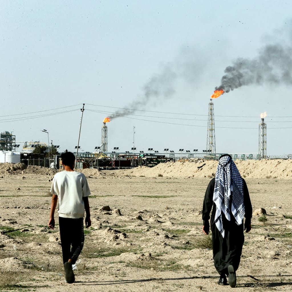 People walk near farmland by the Zubair oil field as gas flares rise in the distance, in Zubair Mishrif, Basra, Iraq, amid regional tensions following the recent disruption to shipping in the Strait of Hormuz and the U.S.-Israeli conflict with Iran on March 9, 2026.