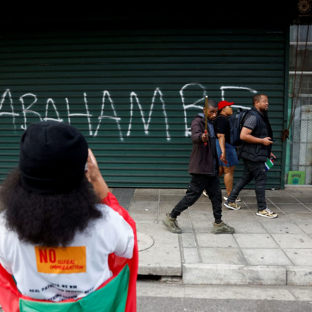 <p>People walk past a slogan reading, “They must go,” written on the shutter of a shop as anti-immigrant protesters march on the day of an unofficial deadline set by anti-immigrant groups for all undocumented migrants to leave, in Durban, South Africa, on June 30, 2026. </p>
