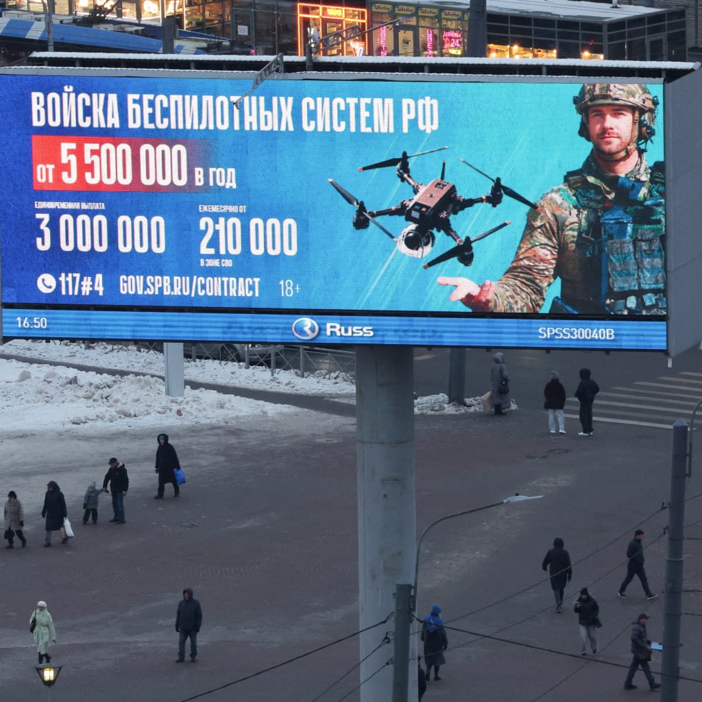 A large digital billboard advertising contract military service in Russia's Unmanned Systems Forces towers over pedestrians crossing a snowy square in St. Petersburg.