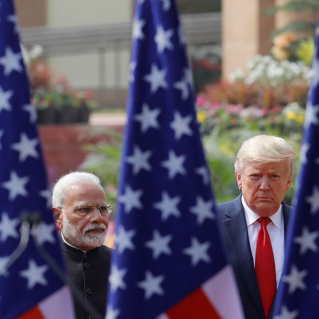 Narendra Modi and Donald Trump face the camera, separated and framed by three U.S. flags.