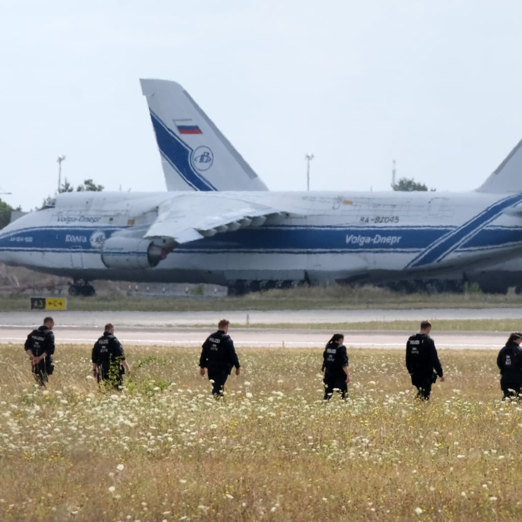 A line of police officers walks through a field of tall grass toward a runway at Leipzig Airport.