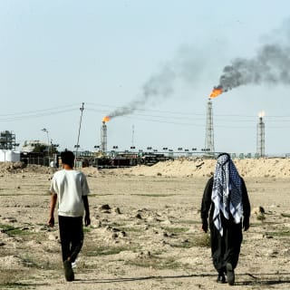 People walk near farmland by the Zubair oil field as gas flares rise in the distance, in Zubair Mishrif, Basra, Iraq, amid regional tensions following the recent disruption to shipping in the Strait of Hormuz and the U.S.-Israeli conflict with Iran on March 9, 2026.