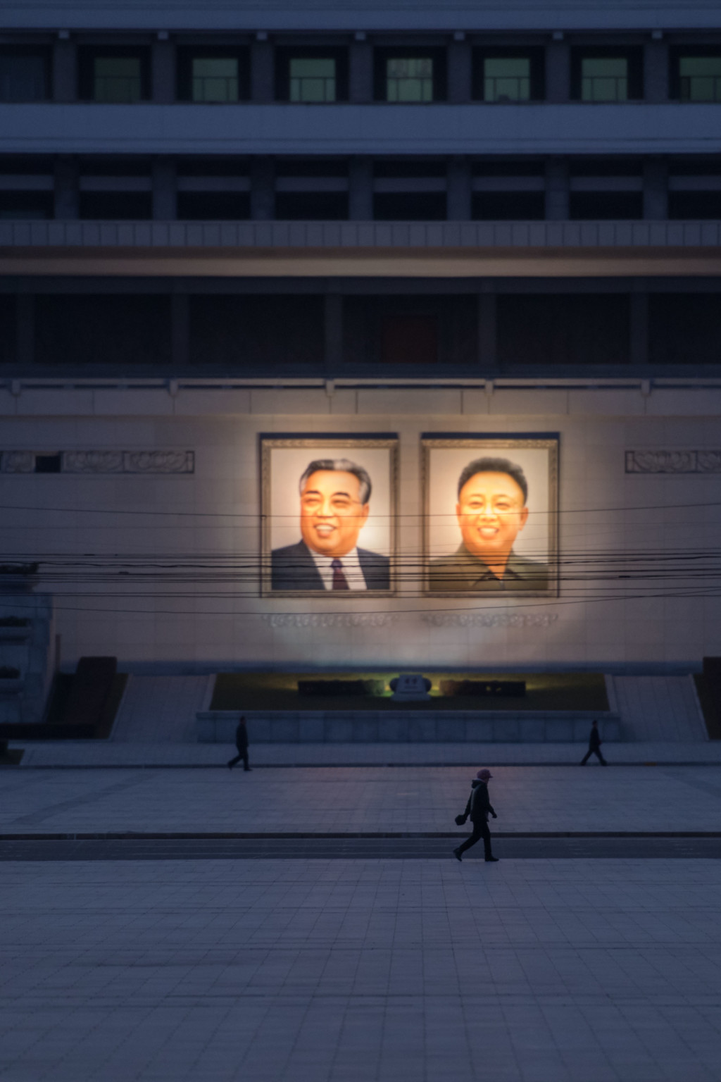 <p>People walk past portraits of Kim Il-sung and Kim Jong-il.</p>
