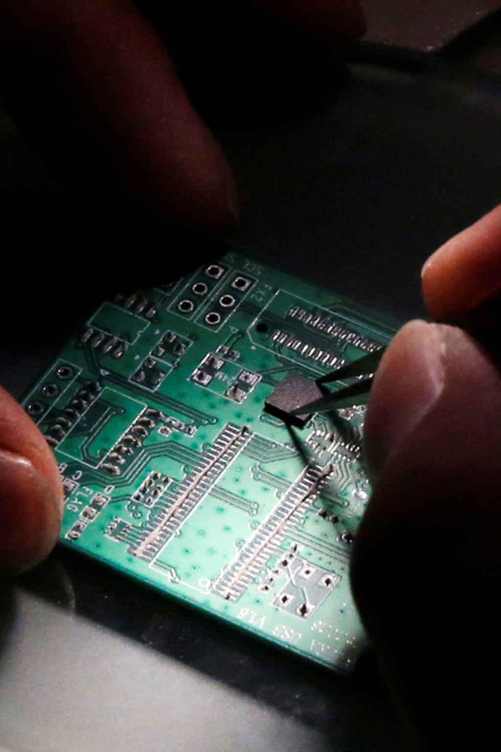 <p>A researcher plants a semiconductor on an interface board, which is placed under a microscope. </p>
