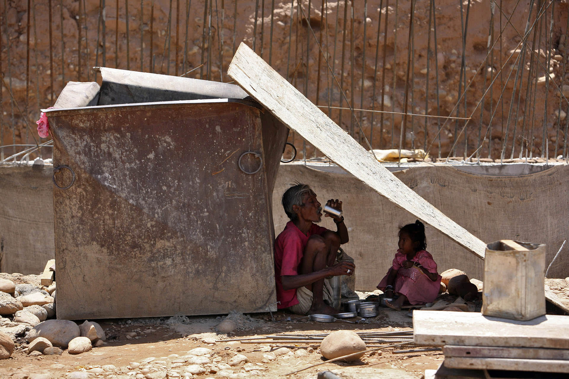 A labourer and his granddaughter eat their meals under a tin shelter on a hot day in Jammu