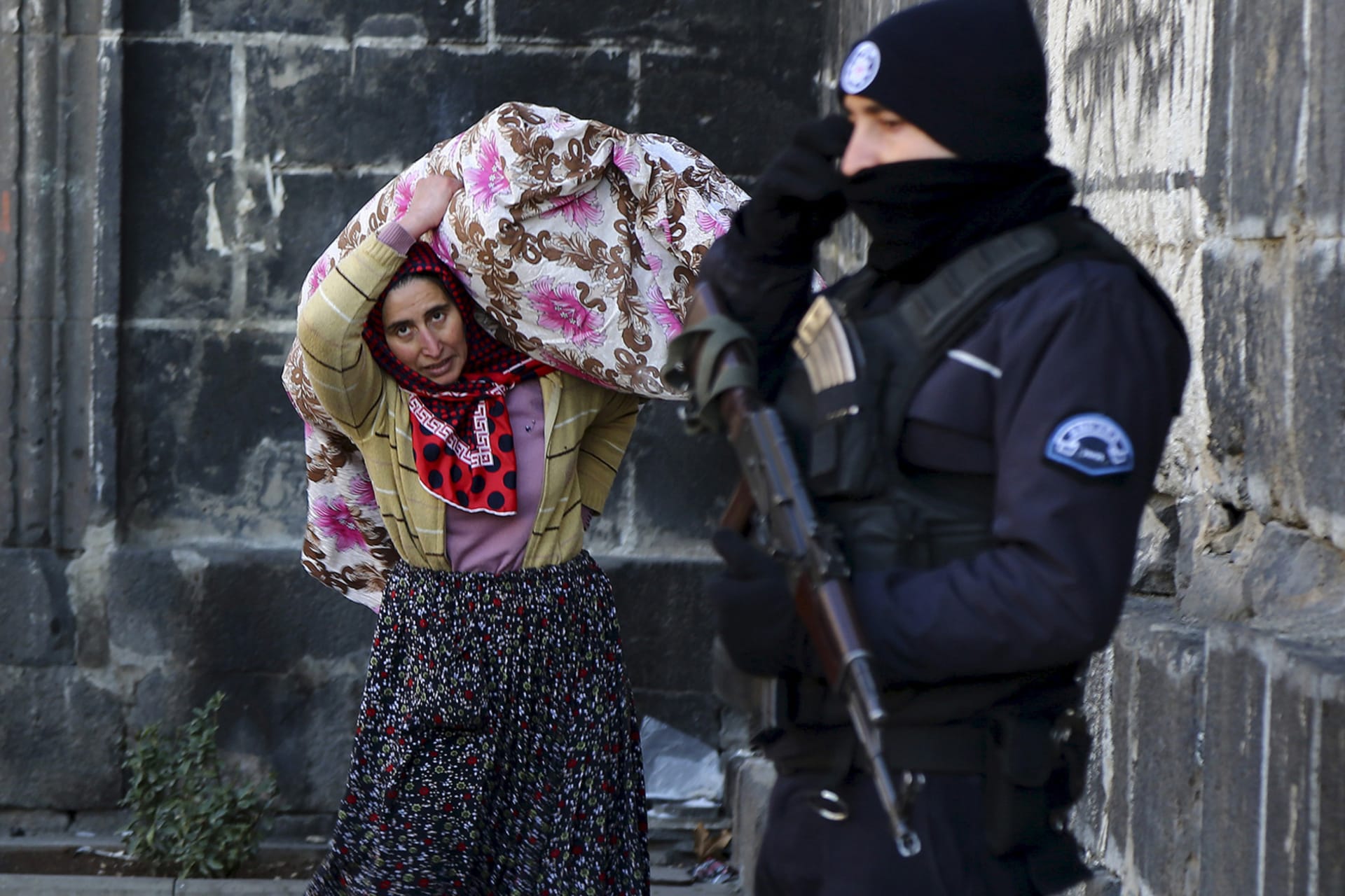 A resident carries her belongings past a police officer as she flees from Sur district, which is partially under curfew, in the Kurdish-dominated southeastern city of Diyarbakir, Turkey on January 27, 2016.
