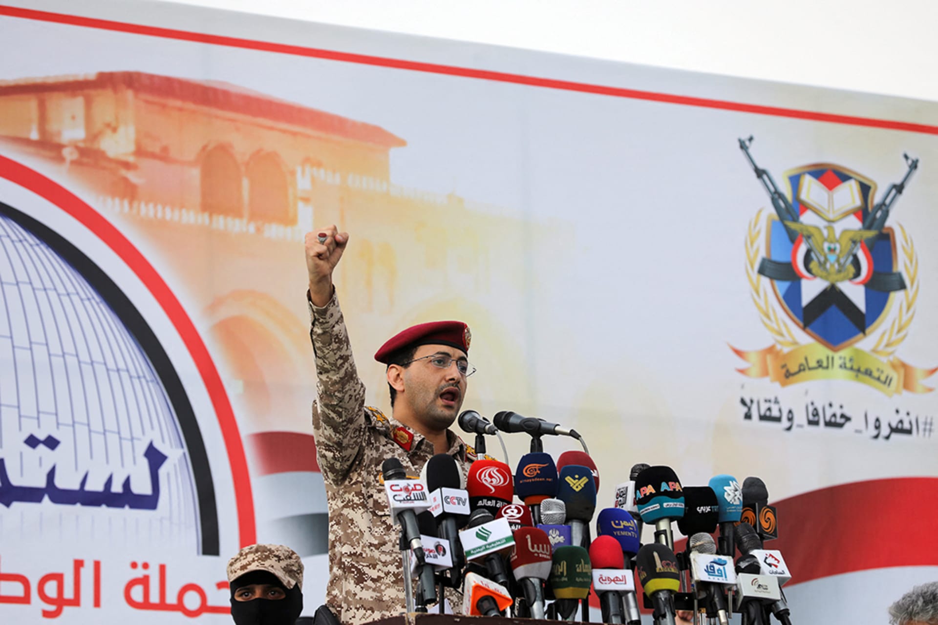 A man wearing military fatigues and a red beret pumps his first in the air while standing at a podium.