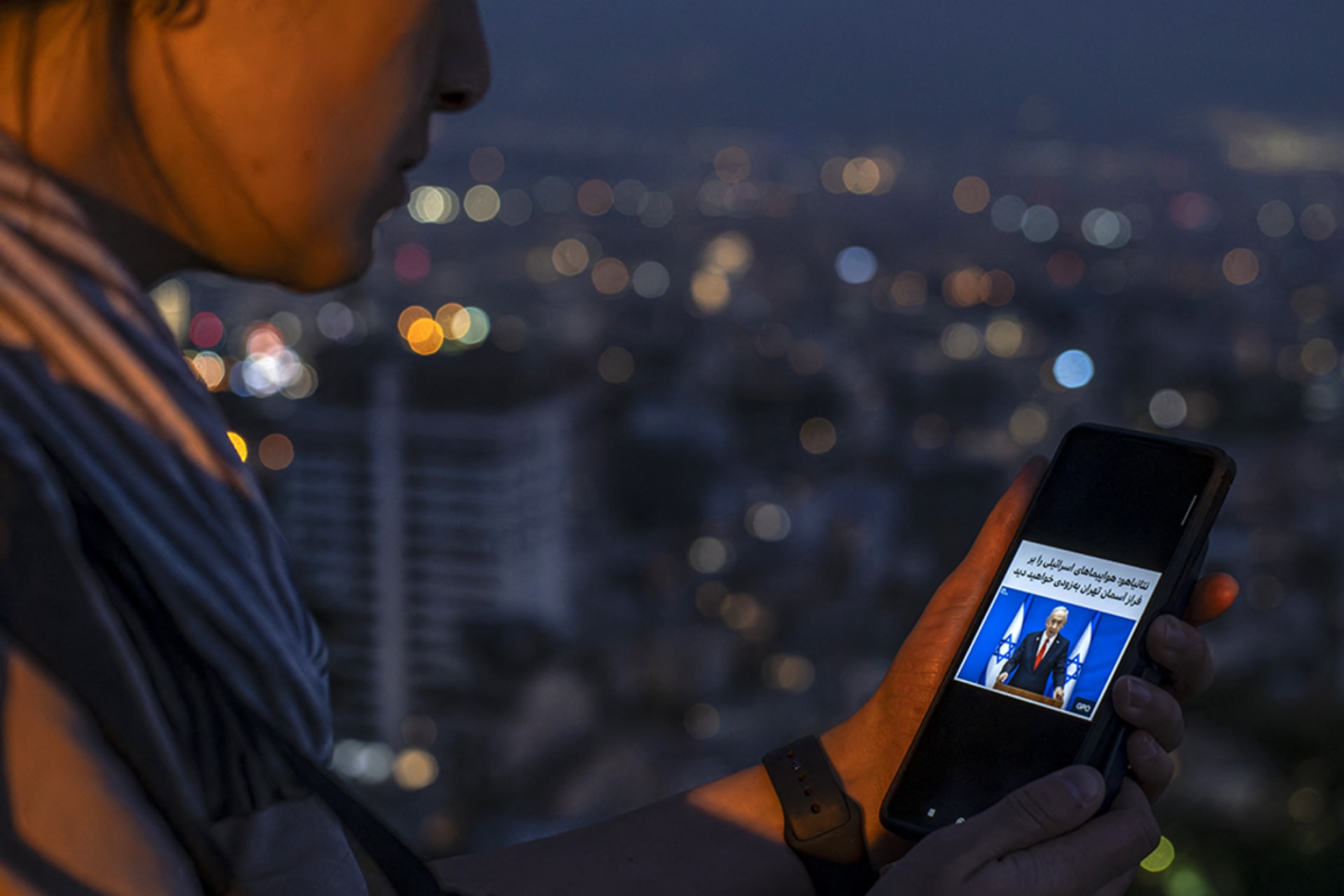 <p>An Iranian girl reads a commentary by the Israeli prime minister saying “you will soon see Israeli jets in Tehran’s sky” on her smartphone as people gather to watch strike exchanges between Israel and Iran on June 14. </p>
