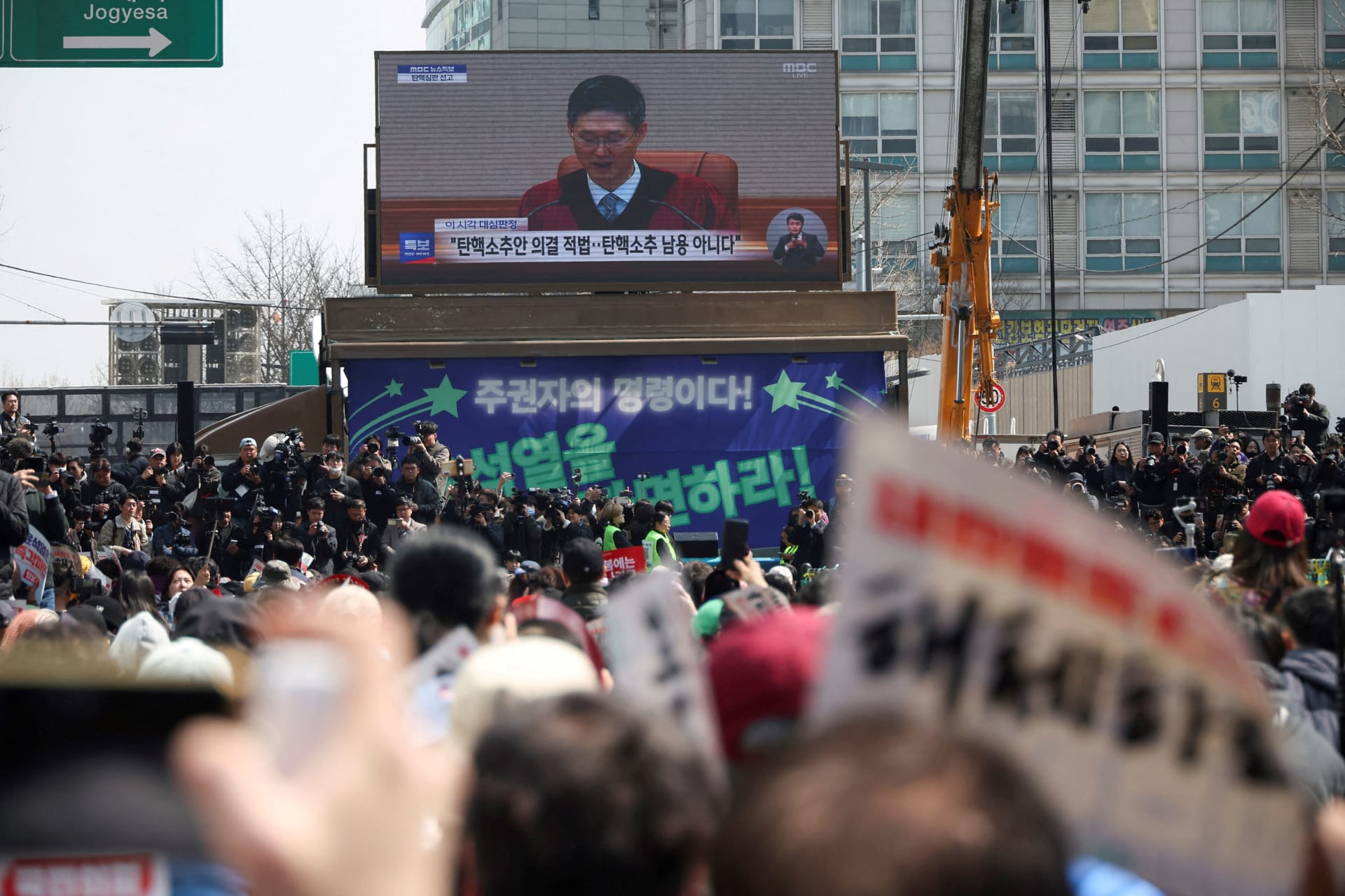 <p>People watch a live news report as they wait for the Constitutional Court ruling on President Yoon Suk Yeol’s impeachment, near the Constitutional Court in Seoul</p>
