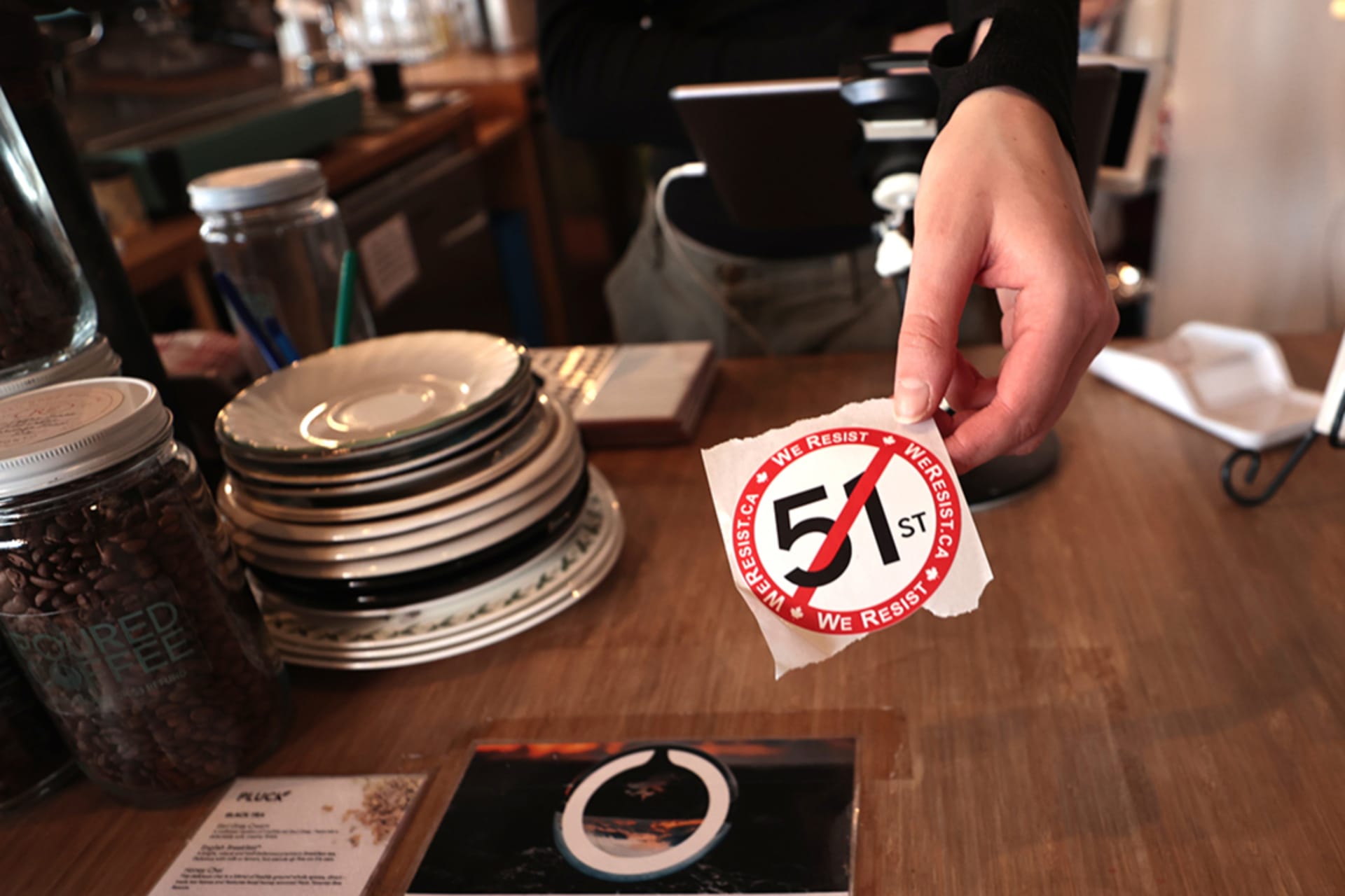 <p>A barista hands out an anti-51st state sticker at a coffee shop in Toronto, Canada, on March 5, 2025.</p>

