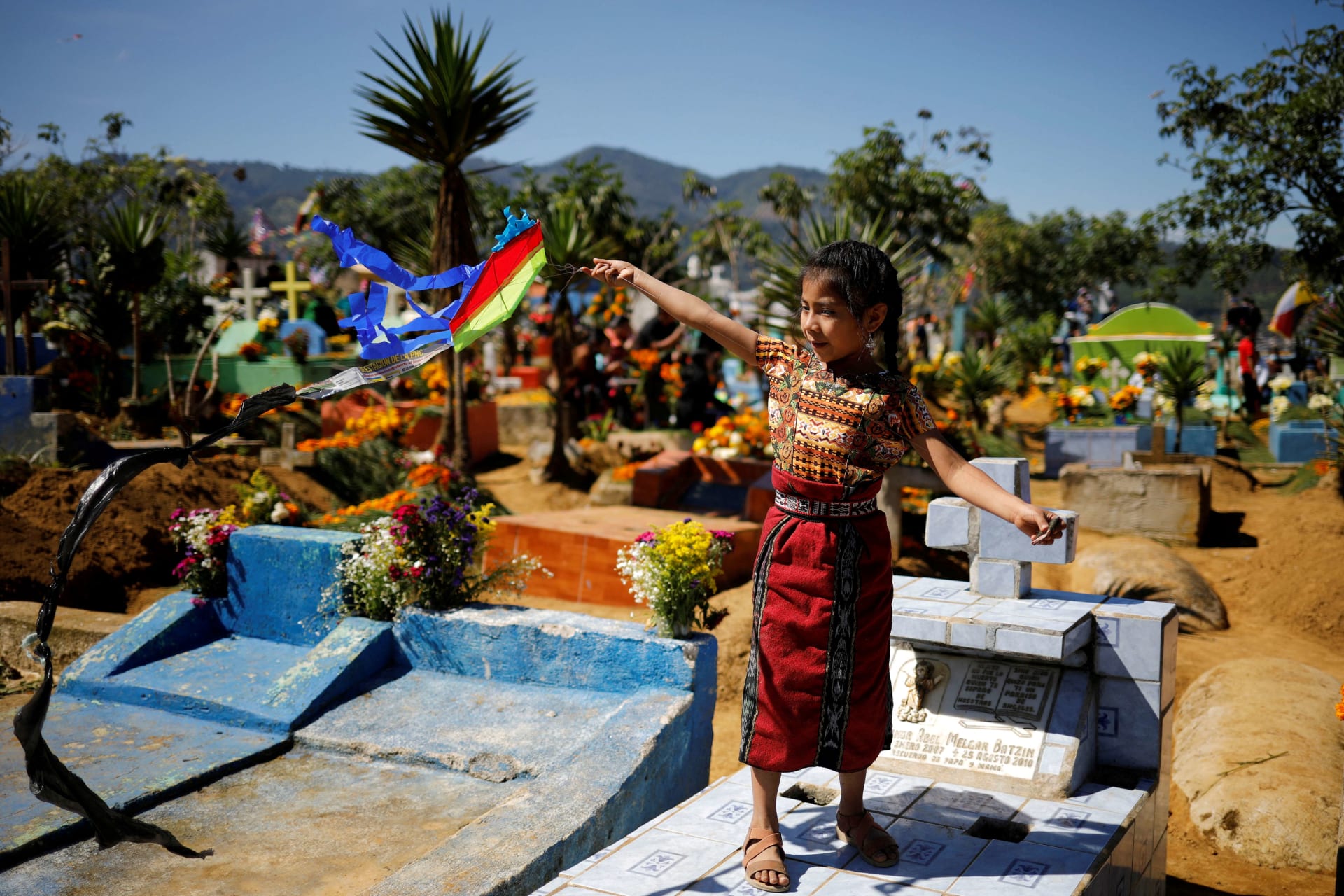 <p>A girl flies a kite over a grave during the celebration of All Saints Day, in Santiago Sacatepequez, Guatemala, November 1, 2022.</p>
