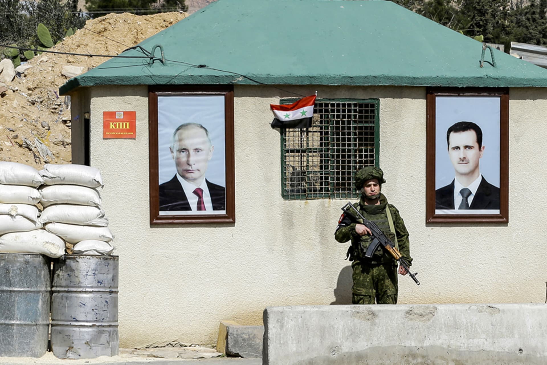 <p>A member of the Russian military police guards a checkpoint on the outskirts of Damascus adorned with portraits of Russian President Vladimir Putin (L) and former Syrian President Bashar al-Assad (R) in March 2018.</p>
