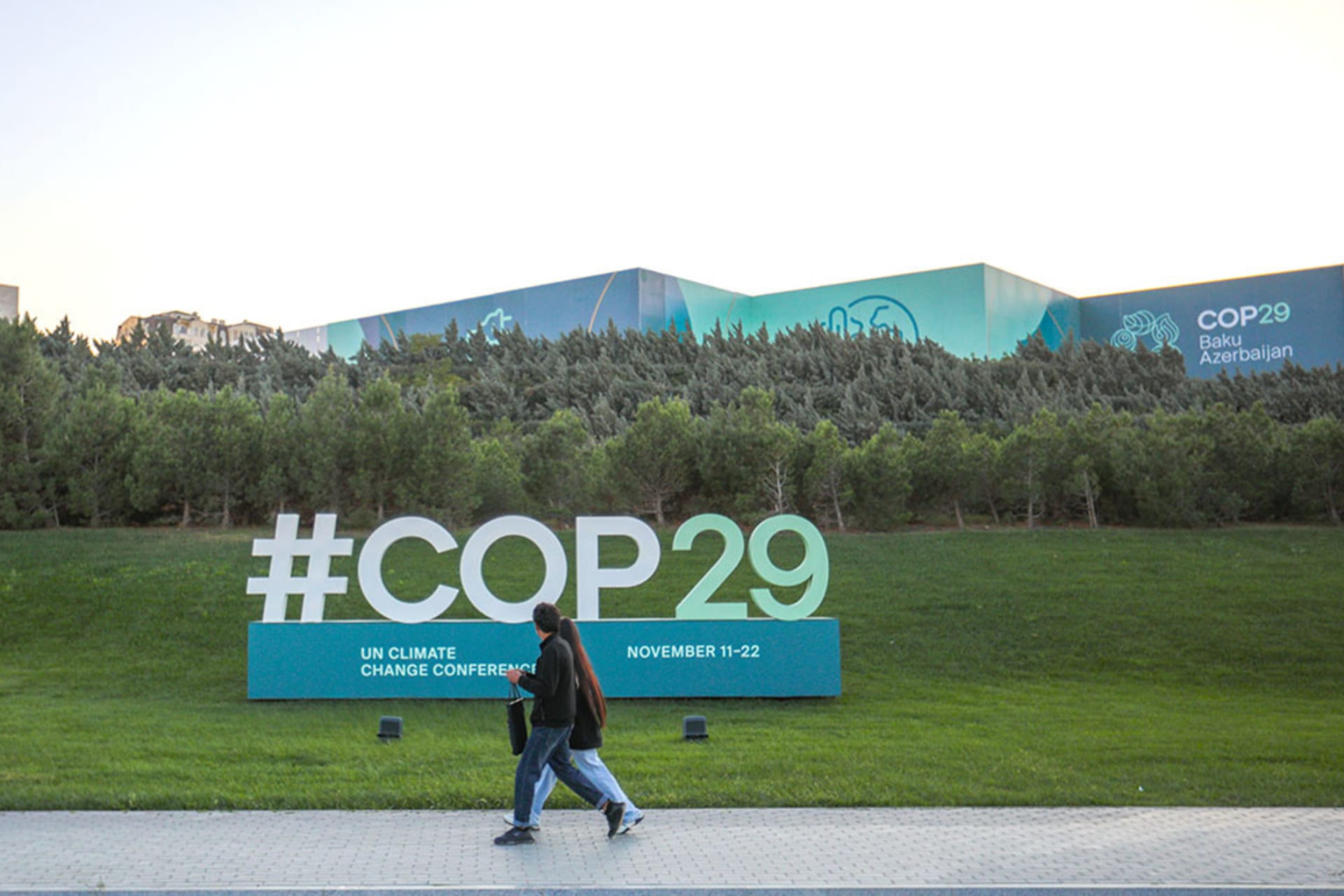 <p>Two people walk near a sign for COP29 near the Baku Olympic Stadium, the venue of the UN climate change conference.</p>
