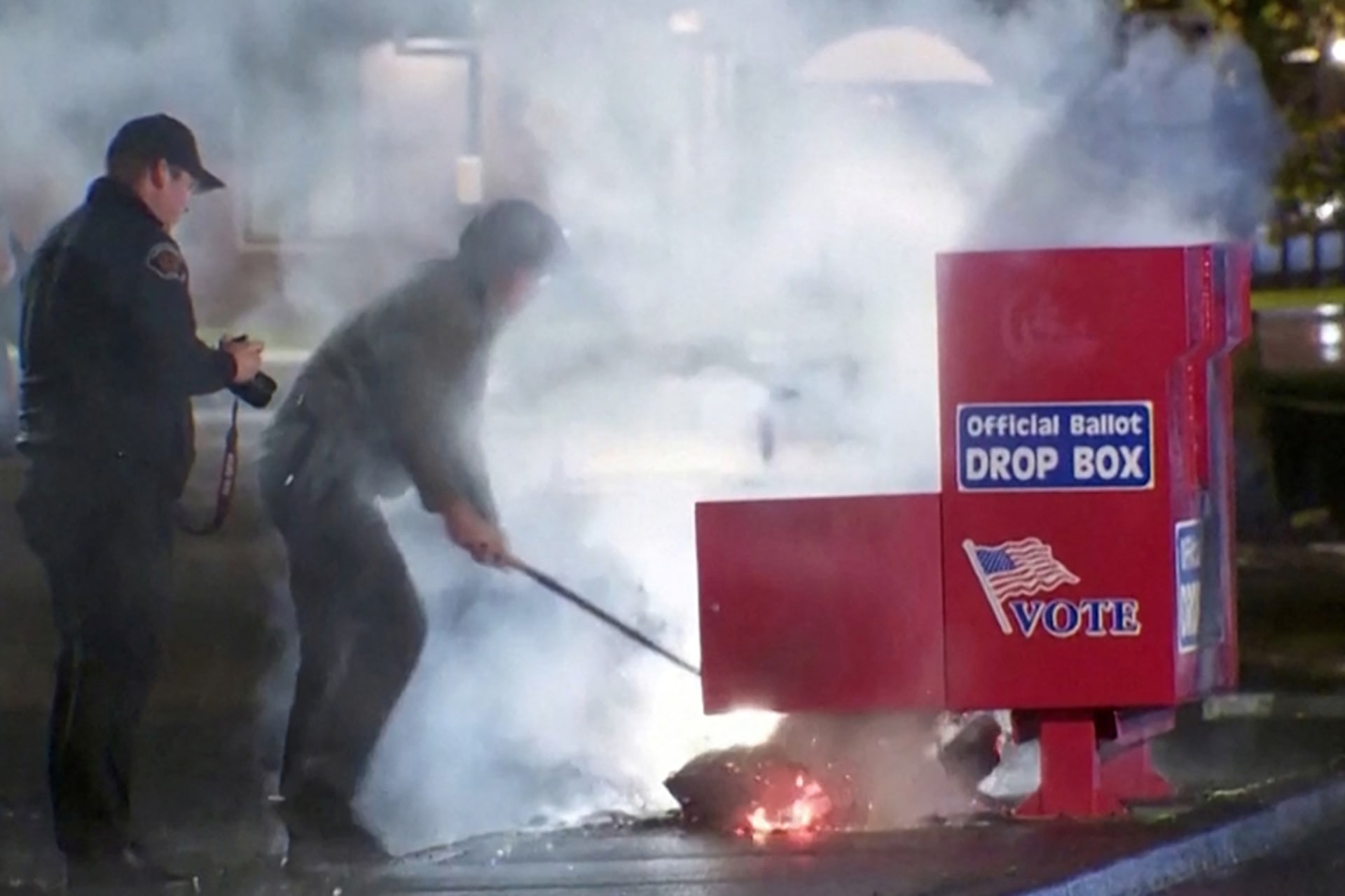 <p>Responders pull out the burning contents of a ballot box after it was set on fire in Vancouver, Washington, in a still image from video.</p>
