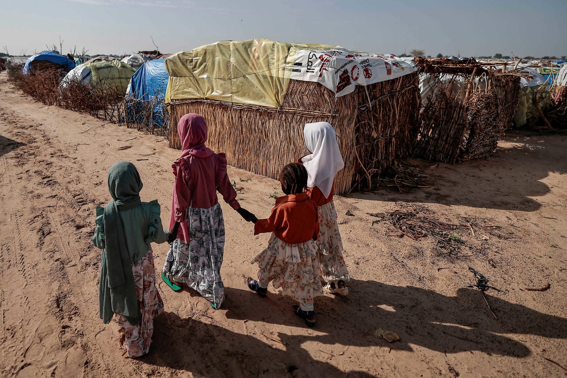 <p>Sudanese girls who fled the conflict in Sudan’s Darfur region, walk beside makeshift shelters holding each other’s hands in Adre, Chad July 29, 2023.</p>
