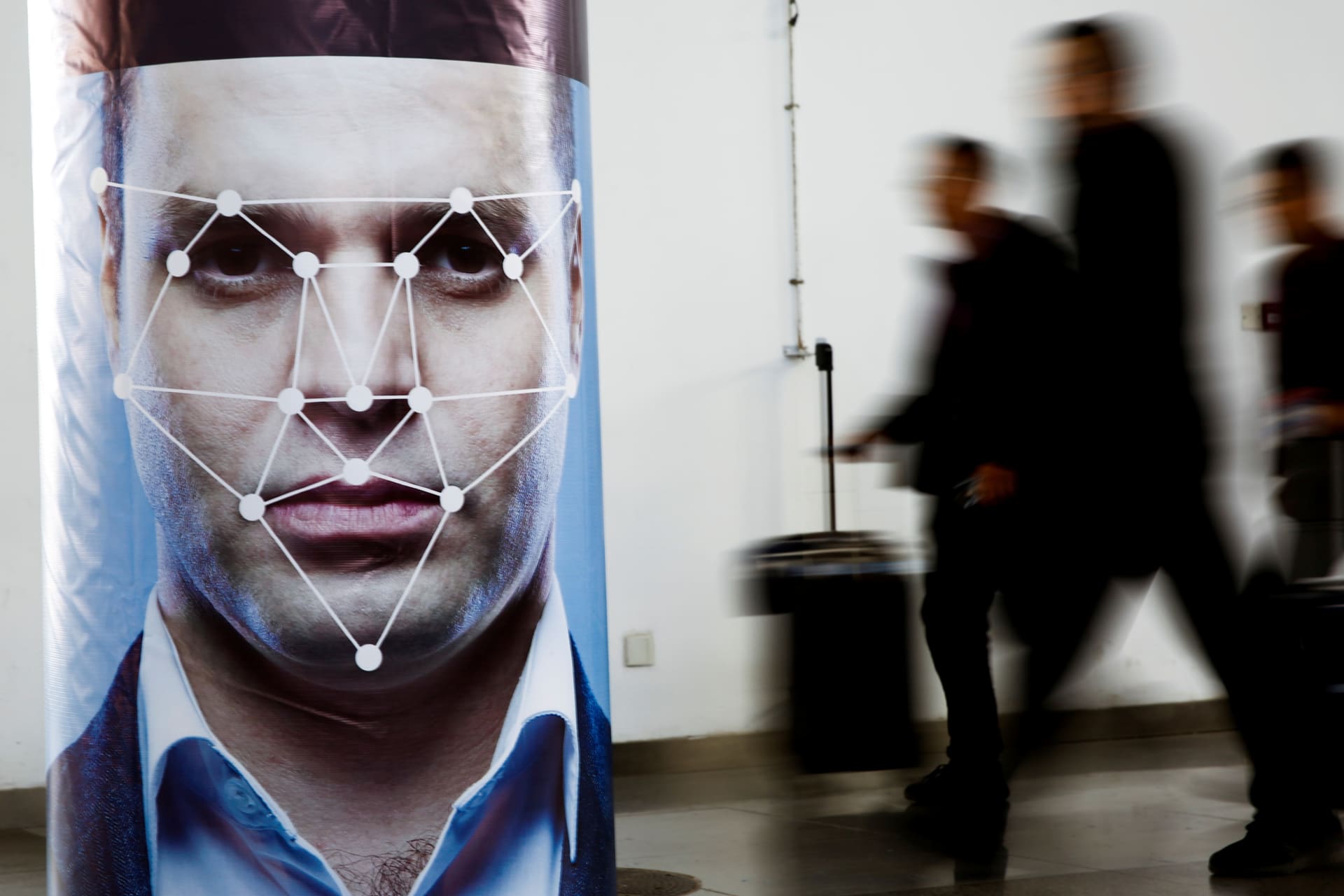 <p>People walk past a poster simulating facial recognition software at the Security China 2018 exhibition on public safety and security in Beijing, China on October 24, 2018</p>
