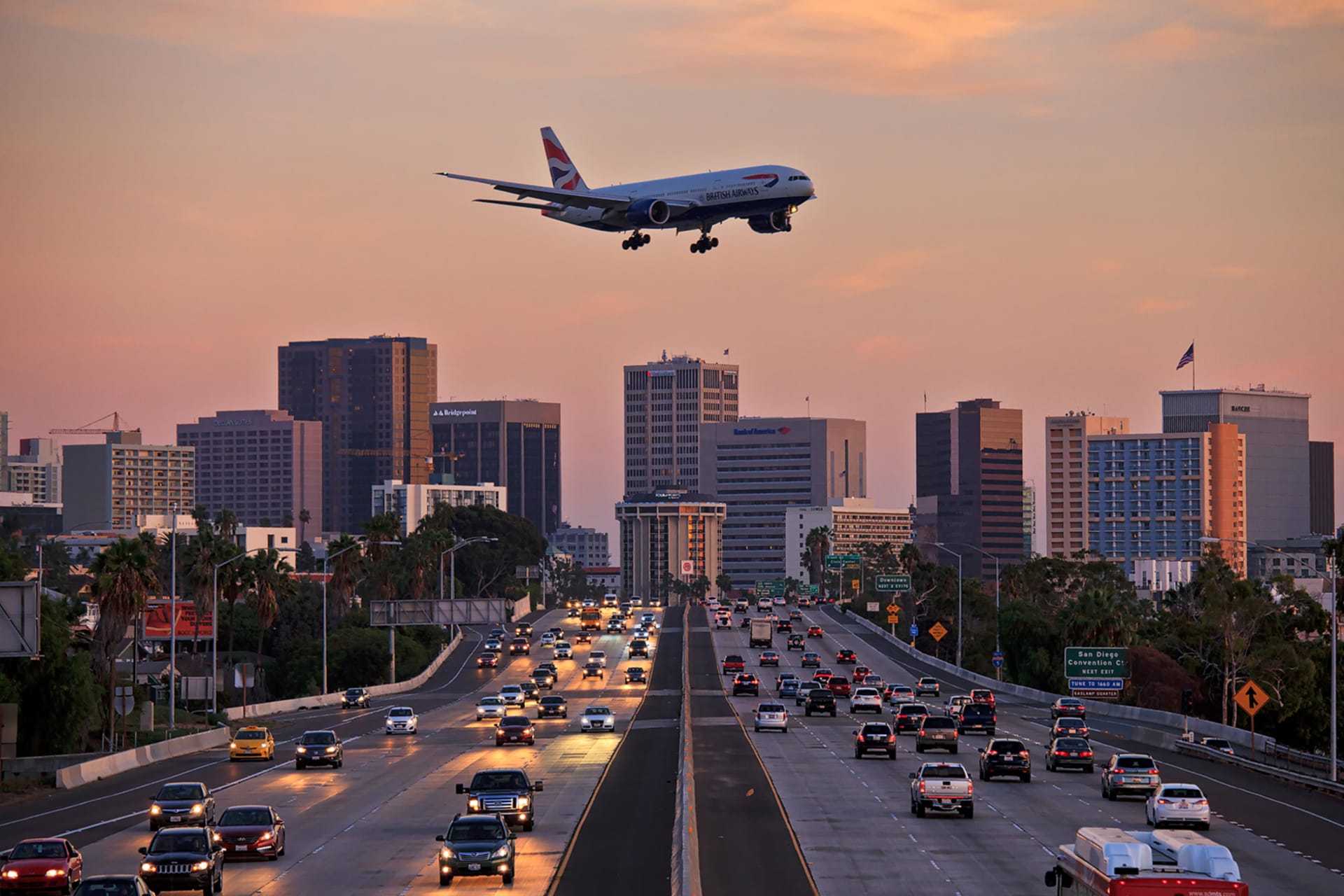 <p>British Airways Boeing 777 flying over crowded freeway to land at Lindberg Field San Diego International Airport.</p>
