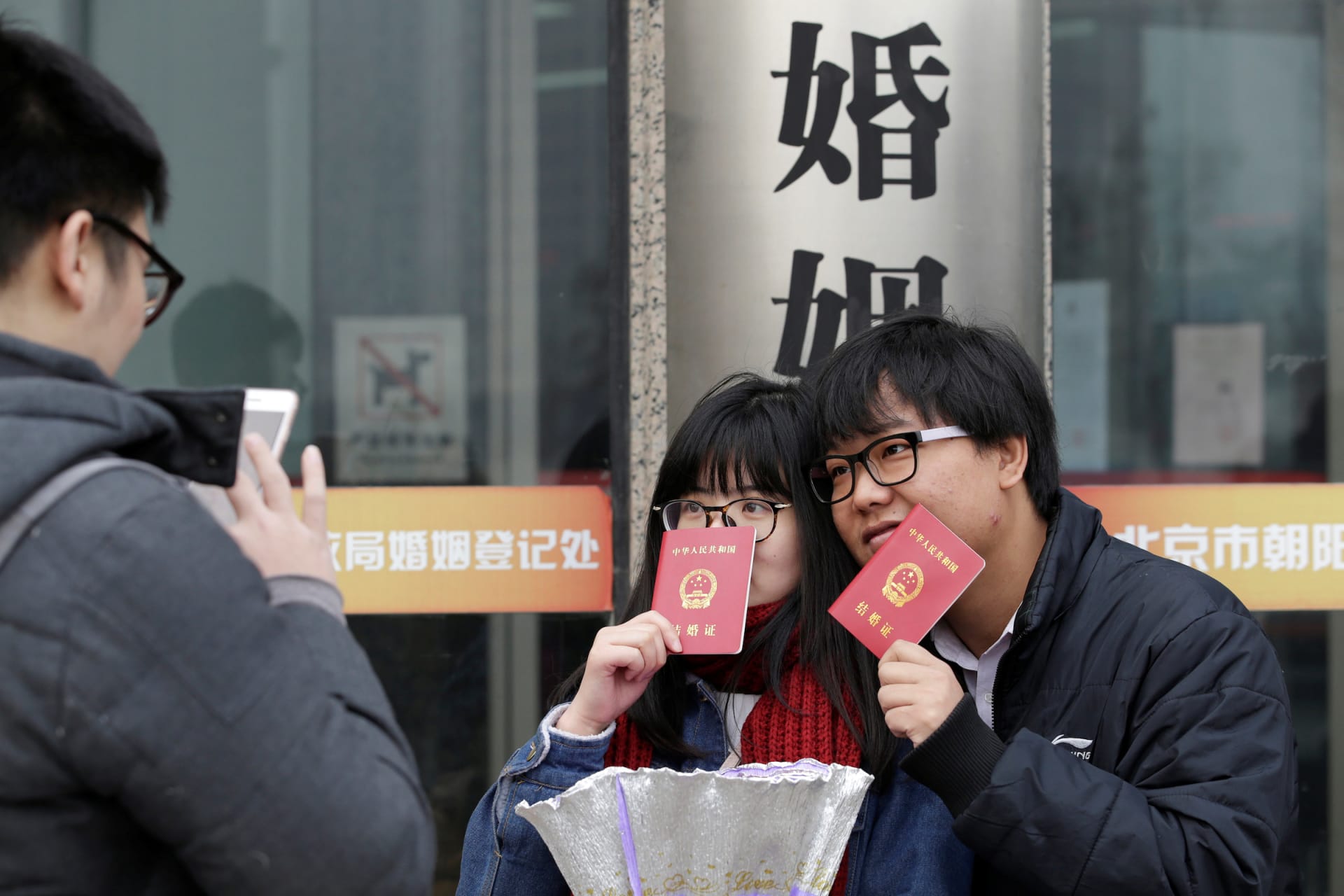 <p>A couple holding marriage certificates poses for a photo outside a registry office of marriage in Beijing, China.</p>
