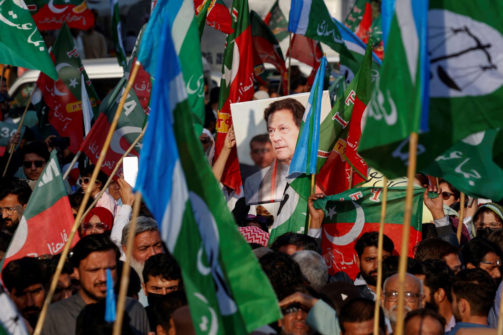<p>A portrait of the former Prime Minister Imran Khan is seen amid flags of Pakistan Tehreek-e-Insaf (PTI) and the Jamat-e-Islami (JI) political parties as supporters attend a joint protest outside the Pakistan Electoral Commission on February 10, 2024.</p>
