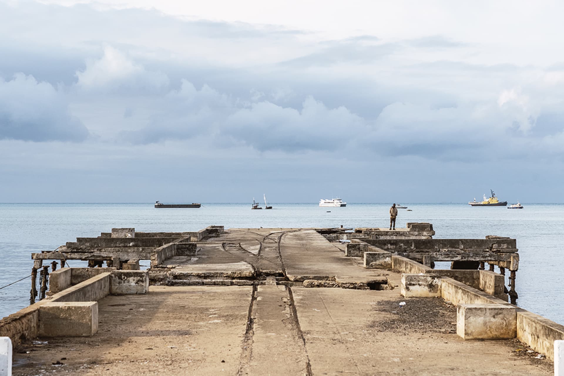 <p>A lone man stands at the end of the old and broken pier watching the boats in the background in the bay of São Tomé city, São Tomé and Príncipe, September 16, 2021.</p>
