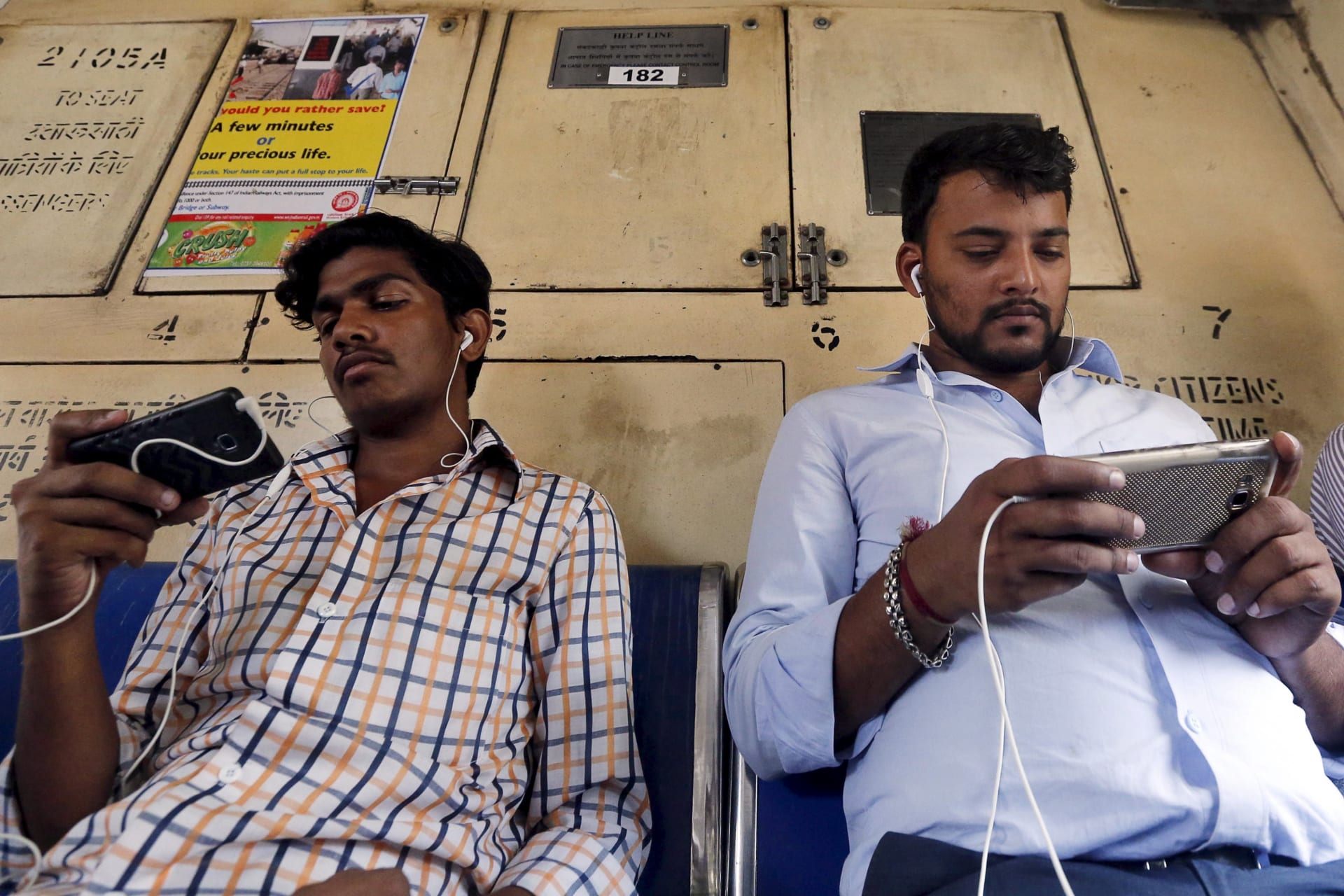 <p>Commuters watch videos on their mobile phones as they travel in a suburban train in Mumbai, India.</p>
