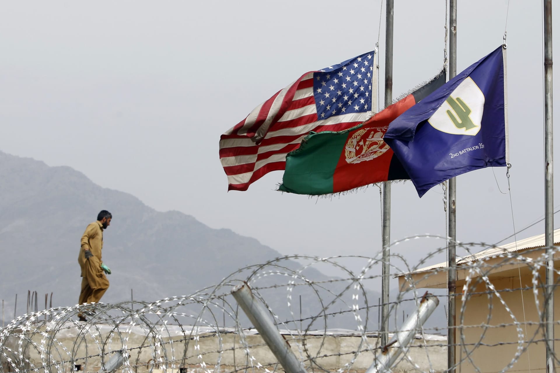 <p>An Afghan working in a U.S military base walks near half mast flags of United States, Afghanistan and Task Force Cacti after a U.S. Army officer was killed by an IED (improvised explosive device) during a patrol in Pesh Valley, at Forward Operating Base J</p>
