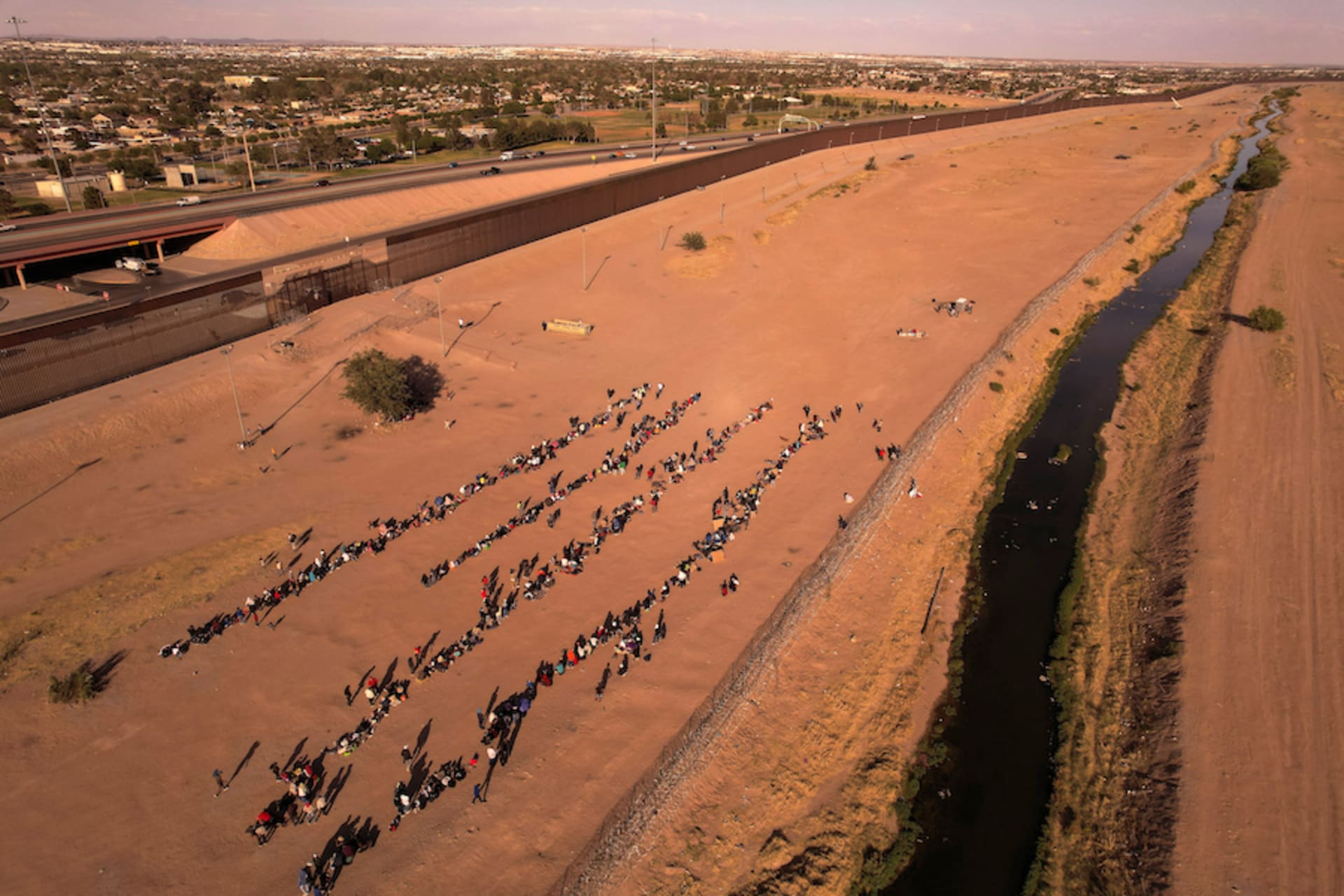 <p>Migrants stand near the border wall after crossing the Rio Bravo river with the intention of turning themselves in to the U.S. Border Patrol agents, as seen from Ciudad Juárez, Mexico.</p>
