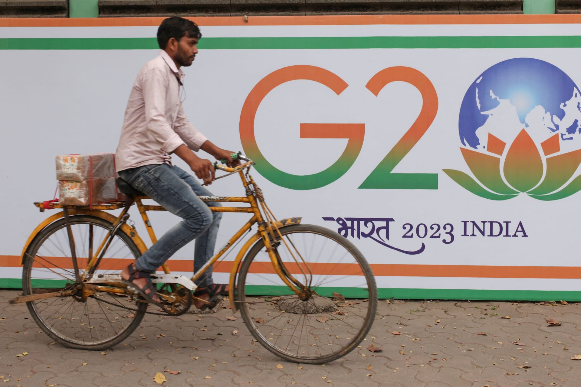 <p>A man rides a bicycle past a poster advertising India’s G20 presidency on a street in Mumbai, India.</p>
