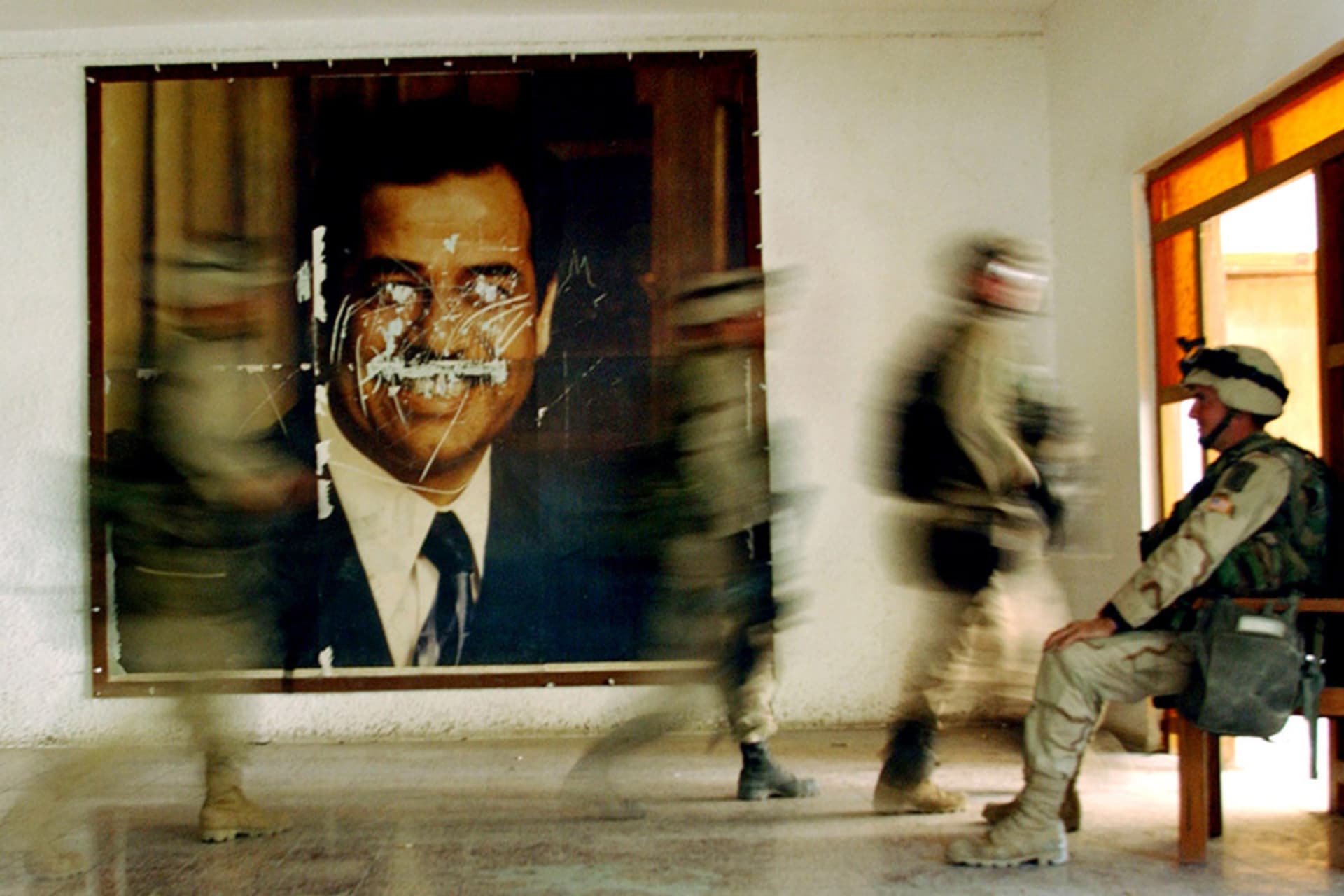 <p>U.S. soldiers walk by a defaced poster of former Iraqi President Saddam Hussein in April 2003.</p>
