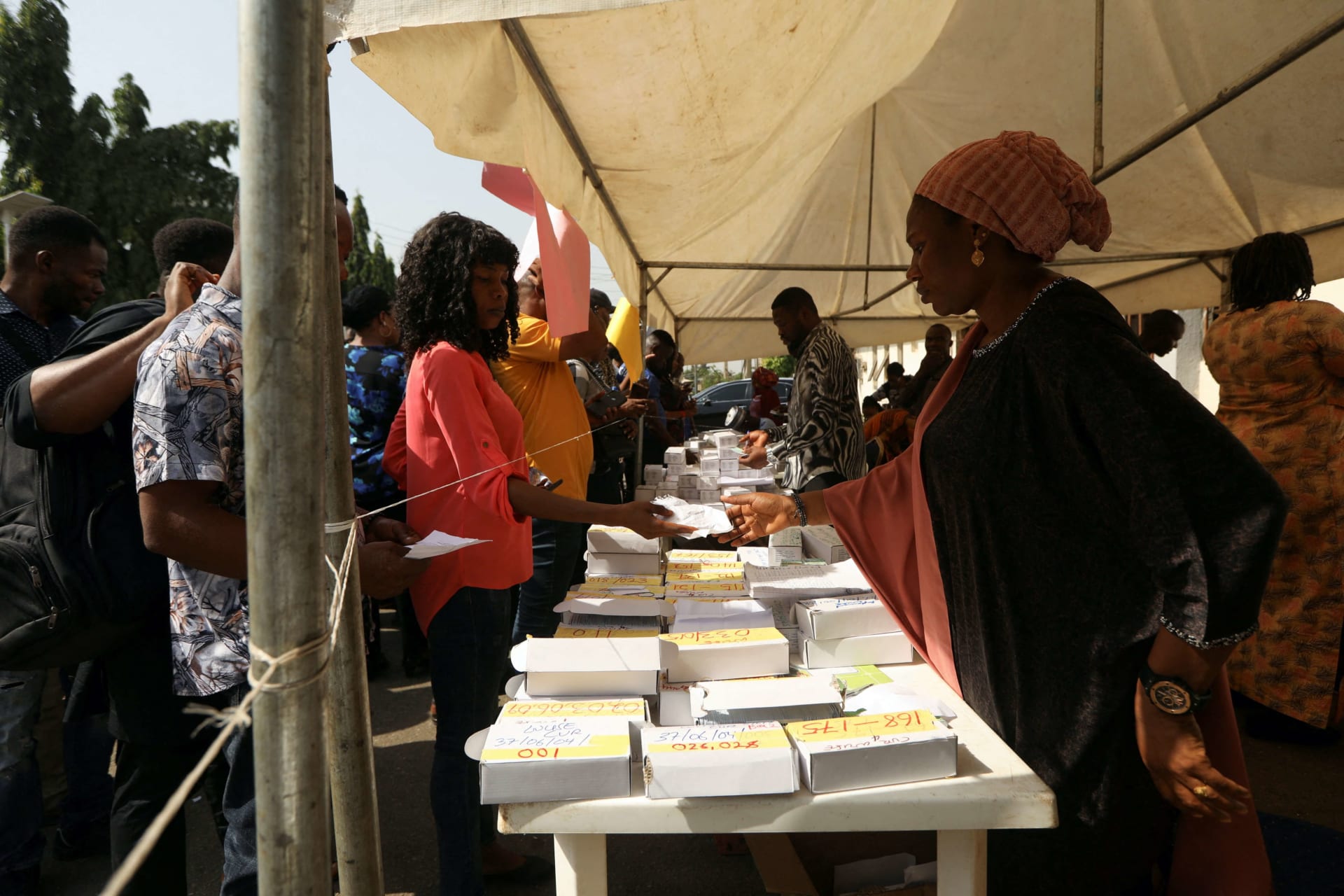 <p>A woman presents a paper to an INEC worker during the collection of permanent voters cards at the INEC office in Abuja, Nigeria on December 13, 2022</p>
