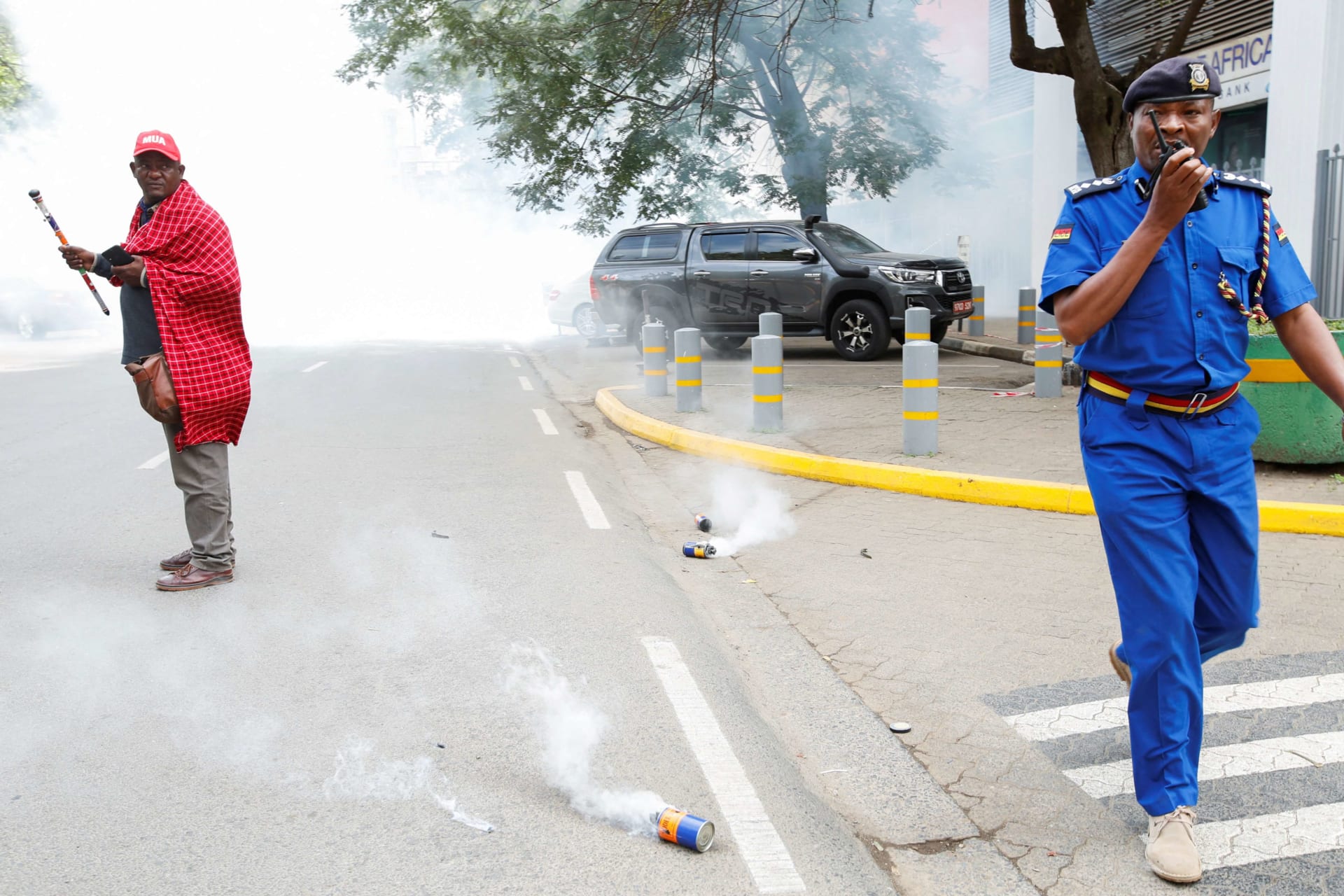 <p>A policeman calls for backup as Jonathan Mpute Ole Pasha, national coordinator of the Maa Unity Agenda (MUA) group in Kenya, stands amid tear gas during a Maasai protest against the eviction of their compatriots in Tanzania on June 17, 2022.</p>
