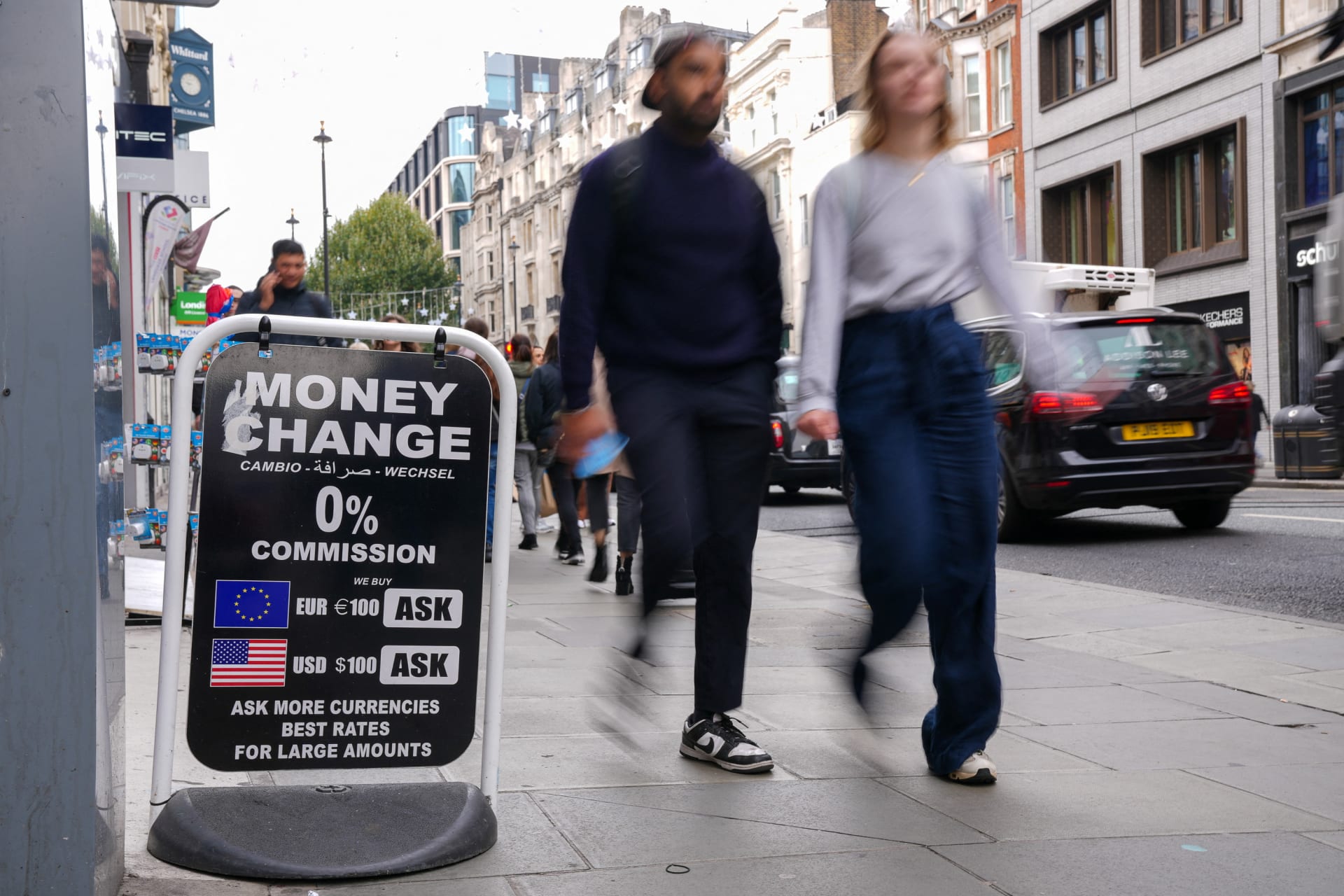 <p>People walk past a sign outside a currency exchange office in London.</p>
