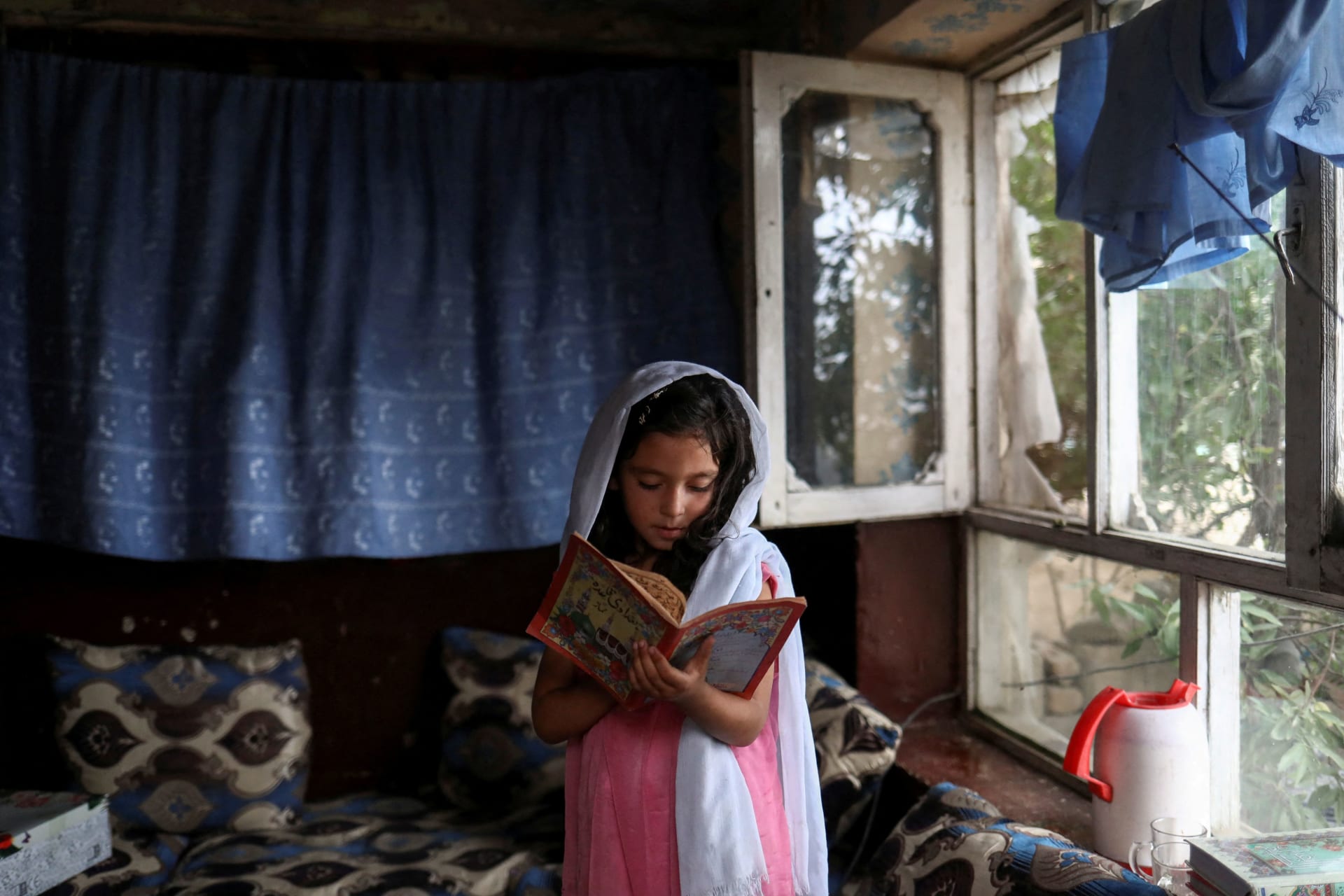 <p>An Afghan girl reads a book inside her home in Kabul</p>
