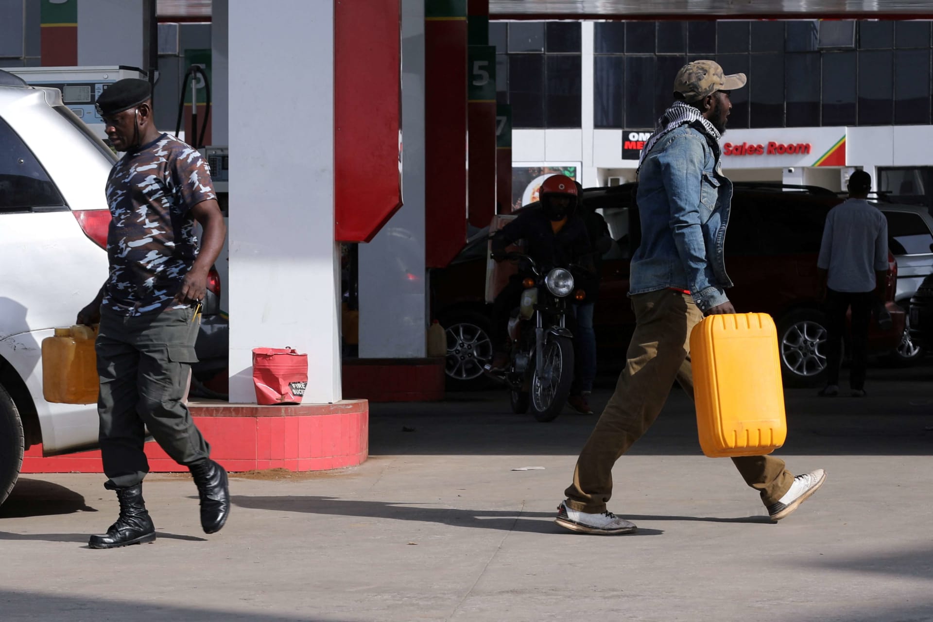 <p>A man and police officer pass one other while carrying petrol containers at a station in Abuja, Nigeria on February 15, 2022.</p>
