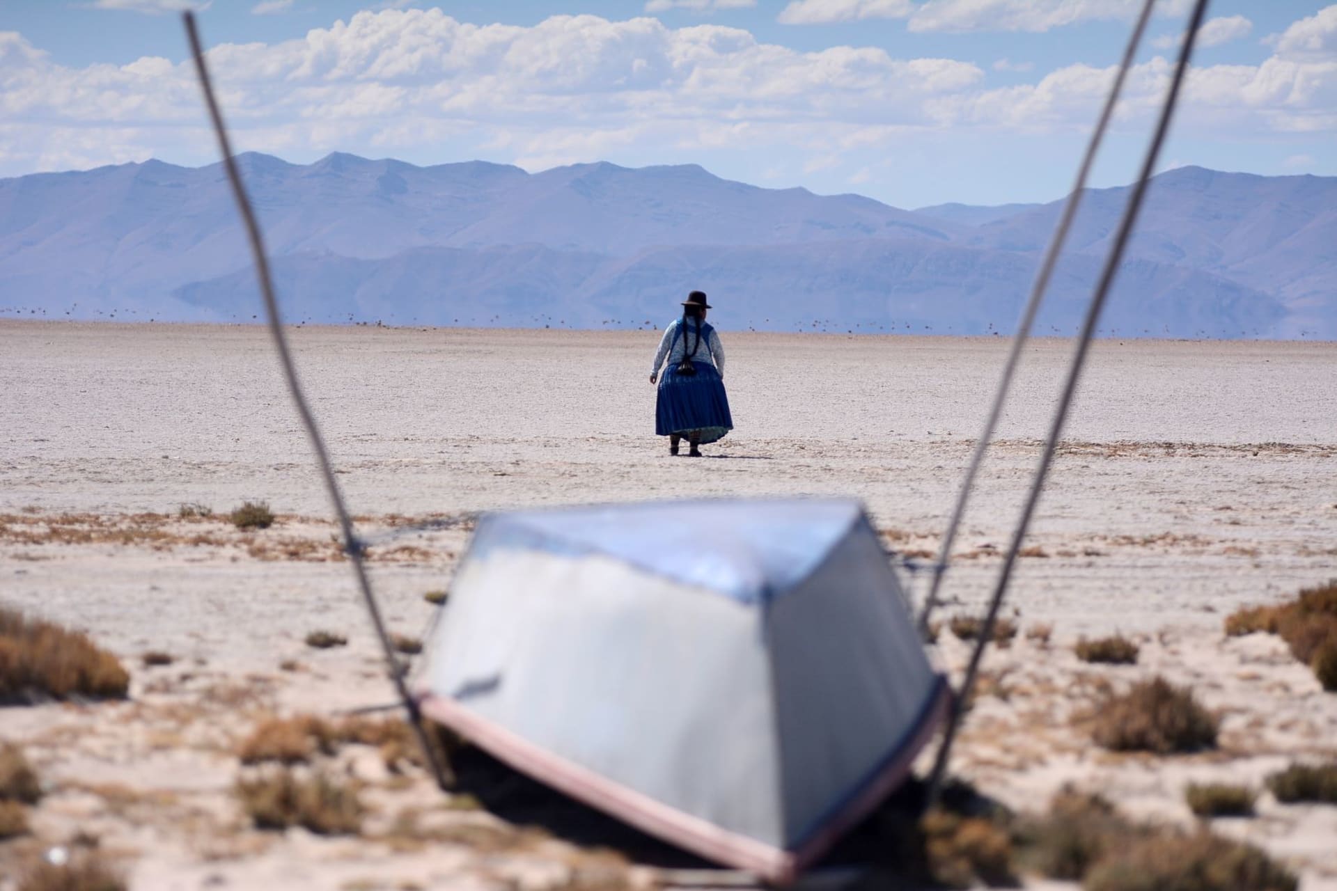 <p>Cristina Mamani walks near an unused boat in Lake Poopo, Bolivia’s second largest lake which has dried up due to water diversion for regional irrigation needs and a warmer, drier climate, according to local residents and scientists on July 24, 2021. </p>
